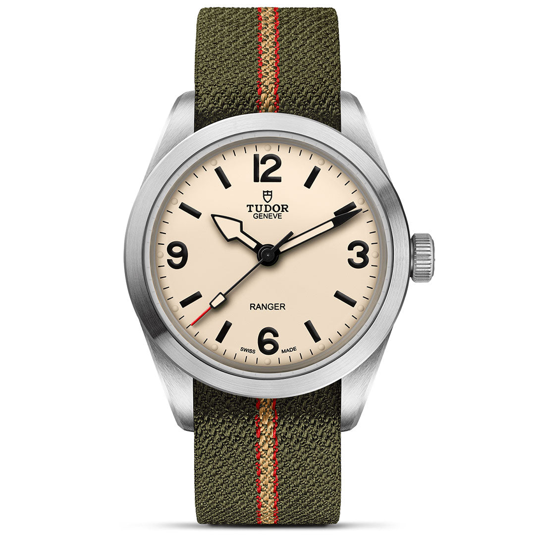 The TUDOR Ranger by TUDOR features a beige dial with black numerals and hands, set in a brushed stainless steel case. It pairs with an olive green fabric strap accented by a red center stripe for rugged style.