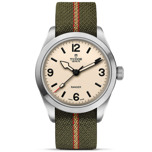 The TUDOR Ranger by TUDOR features a beige dial with black numerals and hands, set in a brushed stainless steel case. It pairs with an olive green fabric strap accented by a red center stripe for rugged style.
