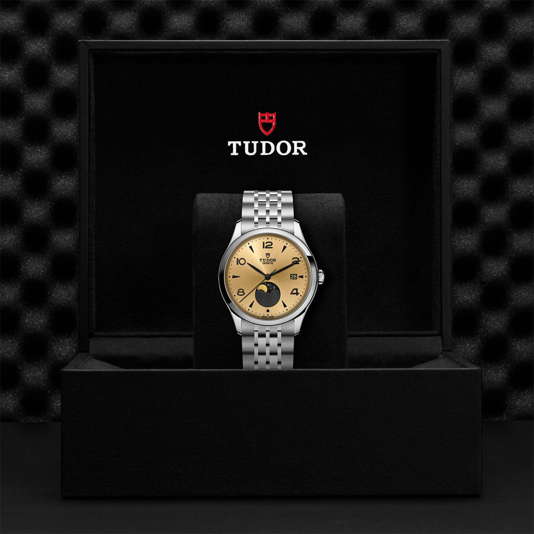 The TUDOR 1926 Luna, a classic elegant wristwatch by TUDOR, features a gold-tone dial and silver bracelet, presented in an open black Tudor-branded watch box with cushioned interior and logo above.