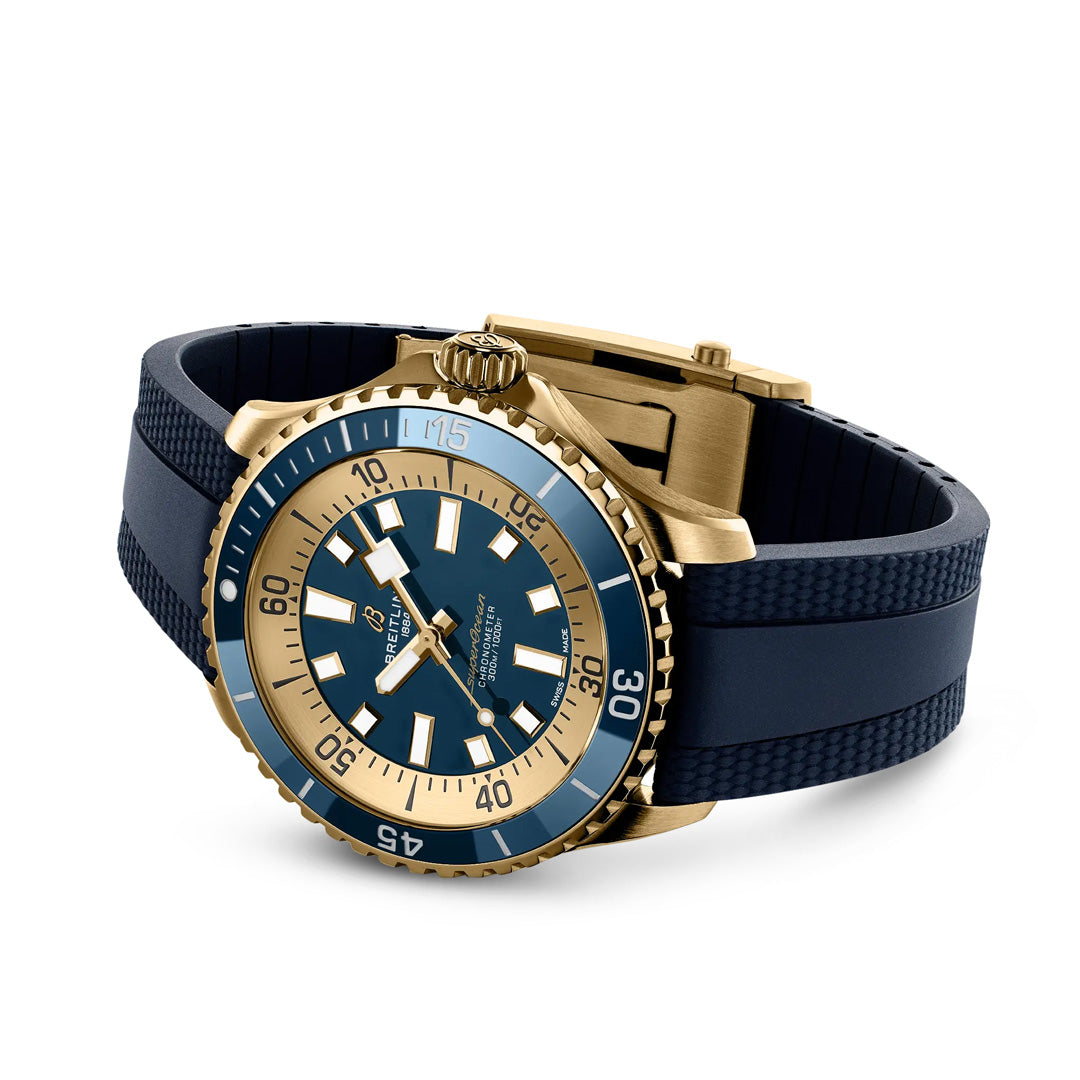 The BREITLING Superocean Automatic 44 dive watch is showcased at an angle, featuring a round blue and gold face, gold bezel, blue rubber strap, bold white numerals, luminescent indexes, and a gold crown. Ideal for scuba diving enthusiasts.