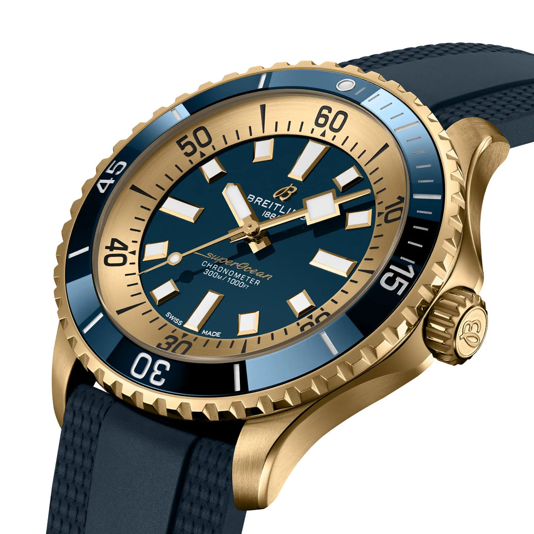 The BREITLING Superocean Automatic 44 is a luxury dive watch with a navy blue dial and gold bezel. It features bold numerals, luminescent indexes, large luminous hands, and a textured navy blue strap. The Breitling brand name is prominently displayed on the dial. Perfect for scuba diving adventures.