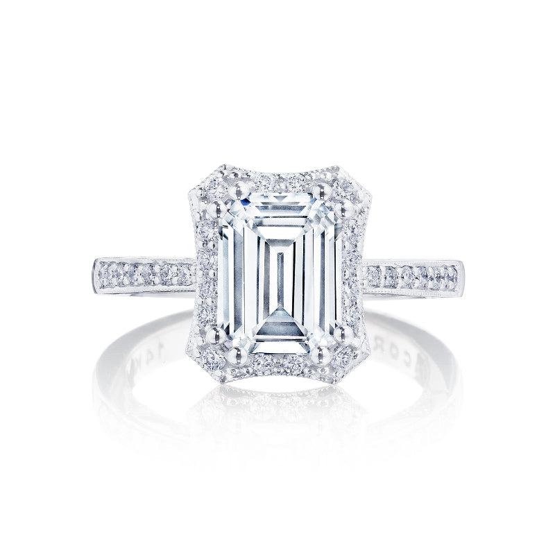 The Tacori Coastal Crescent engagement ring showcases an exquisite emerald-cut diamond at its center, complemented by a halo of smaller G-H color, SI1 clarity diamonds along the band and setting. This stunning 14K white gold ring by Tacori is elegantly presented against a plain white background.
