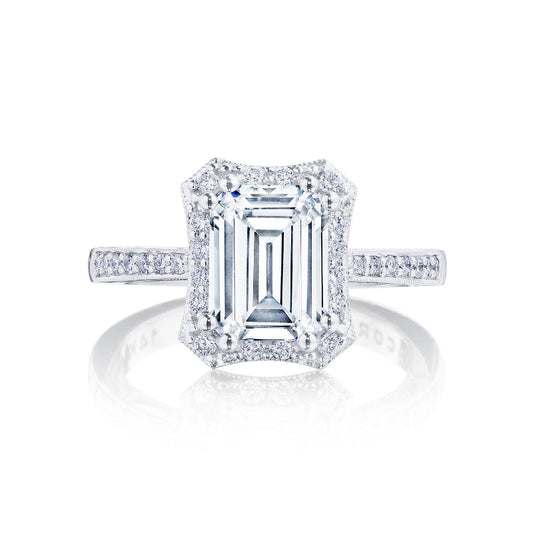 The Tacori Coastal Crescent engagement ring showcases an exquisite emerald-cut diamond at its center, complemented by a halo of smaller G-H color, SI1 clarity diamonds along the band and setting. This stunning 14K white gold ring by Tacori is elegantly presented against a plain white background.