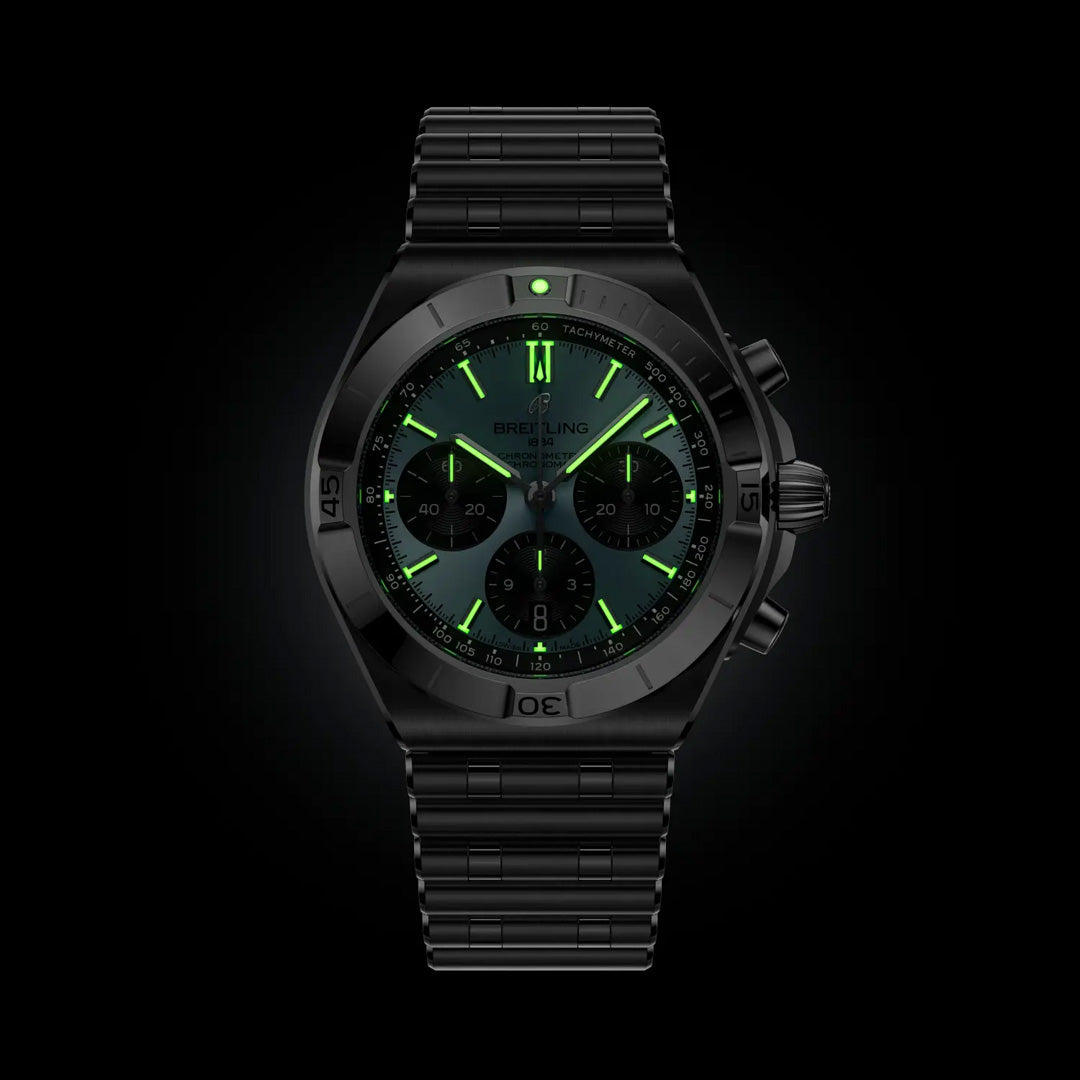 The BREITLING Chronomat B01 Chronograph 42 by Breitling features a black dial and metal band, glowing in the dark with bright green luminous hour markers, hands, and subdials that highlight its chronograph functions.