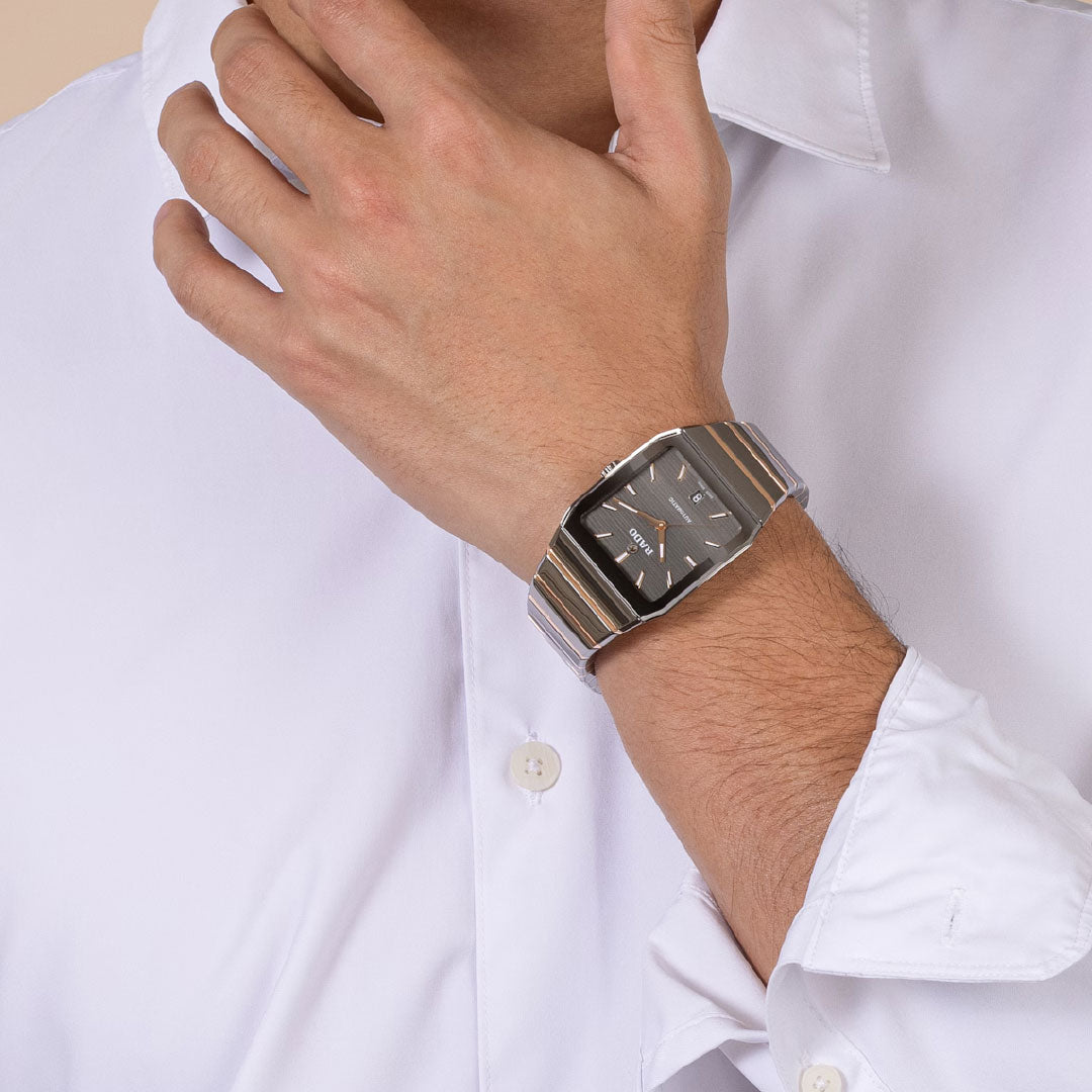 A person in a white dress shirt wears the RADO Anatom Automatic 32.5mm watch, featuring a black face and sapphire crystal, while holding their hand near their chin.