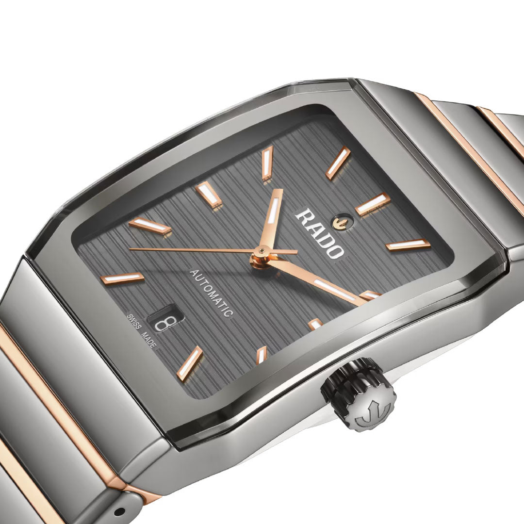 A close-up of the RADO Anatom Automatic 32.5mm watch featuring a rectangular face, rose gold markers and hands, gray textured dial, sapphire crystal, date window at 6 o’clock, and a silver/rose gold metal bracelet.