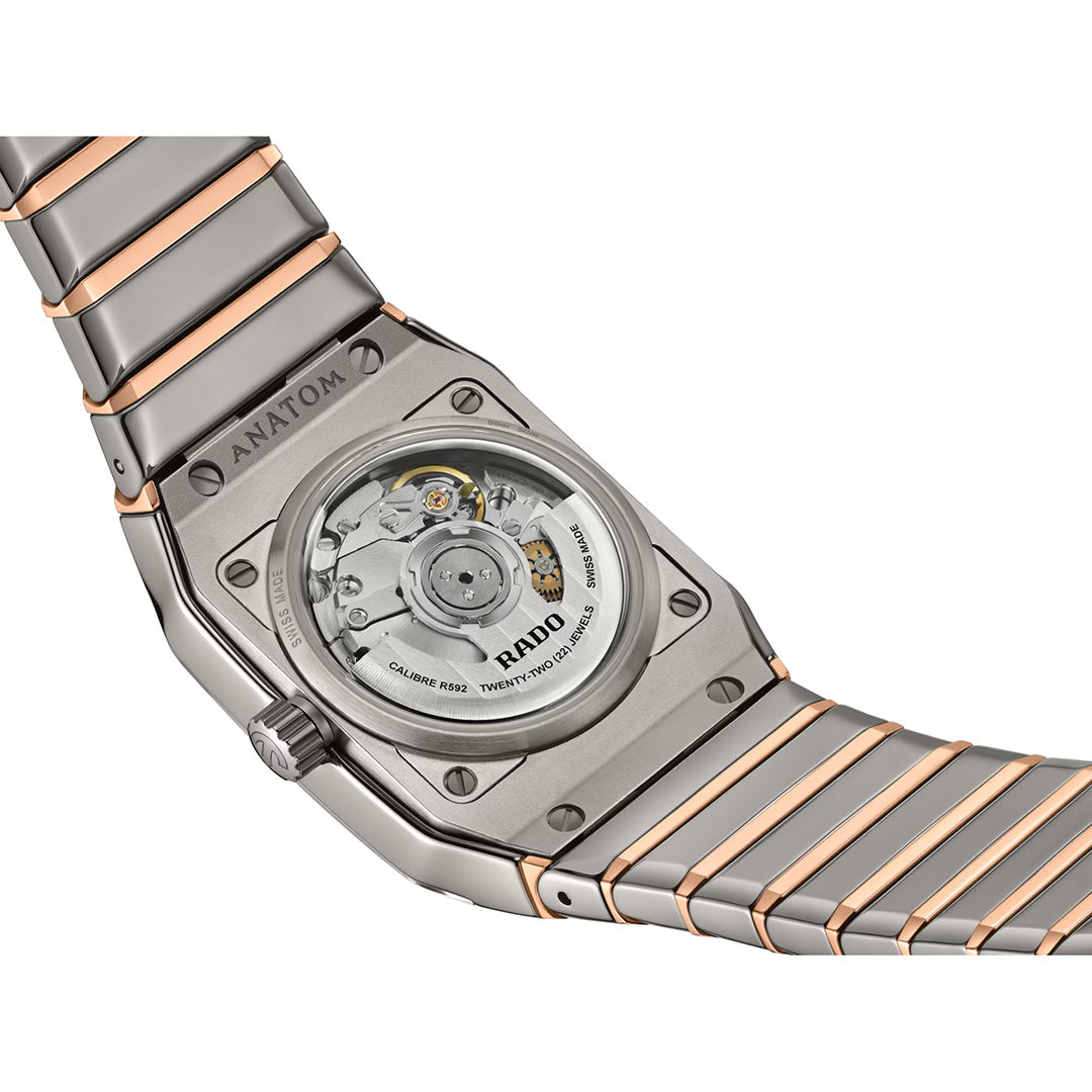 Close-up of the back of the RADO Anatom Automatic 27.5mm Watch, showcasing its exposed automatic movement through a transparent case back. The watch features a sleek silver and rose gold metal bracelet, demonstrating RADO’s innovation and design expertise seen in timepieces such as those in their high-tech ceramic watch collection.