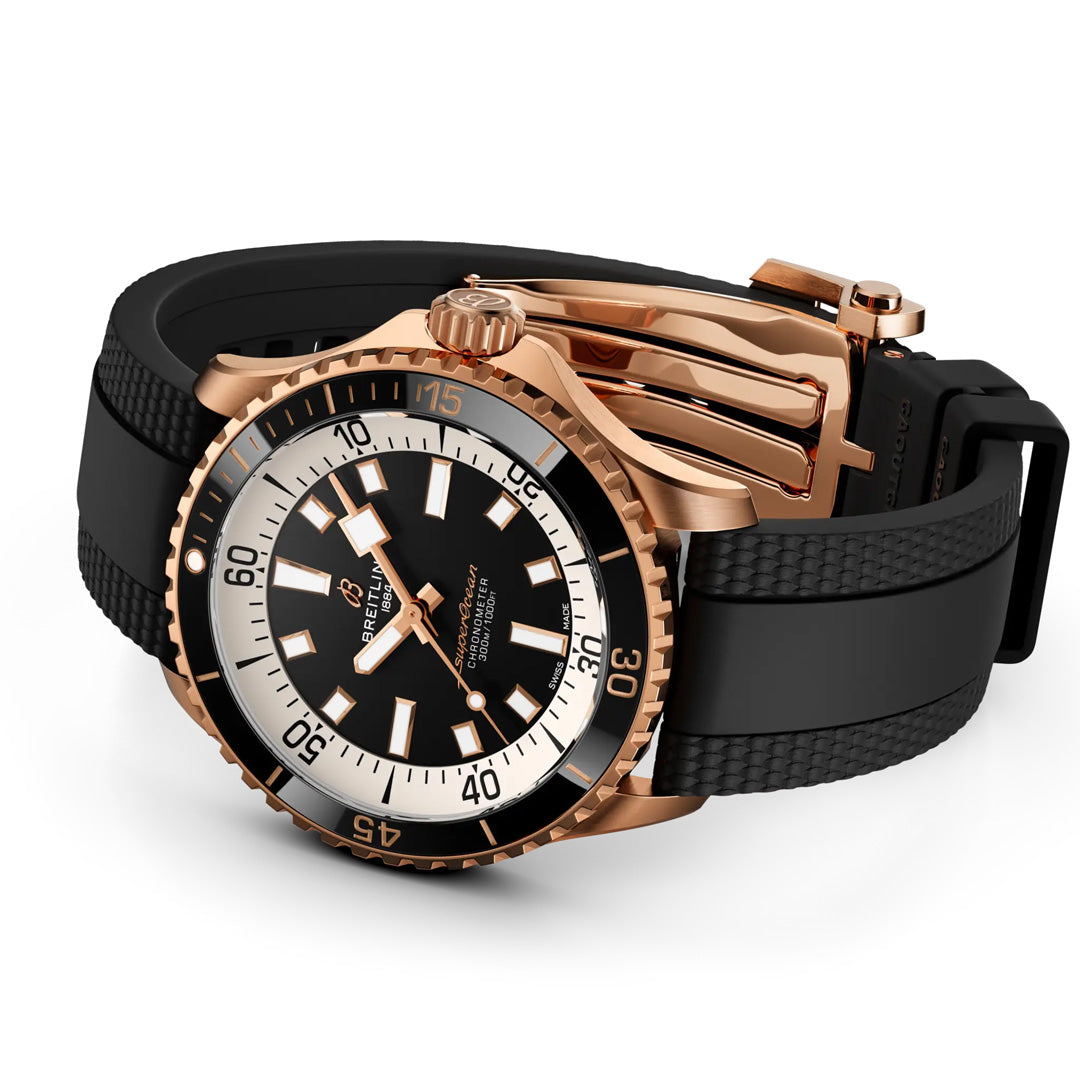 The BREITLING Superocean Automatic 42 by Breitling features a rose gold case, a striking black and white dial with bold hour markers, and a black rubber strap, all showcased against a white background.