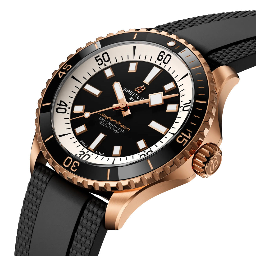 The BREITLING Superocean Automatic 42 by Breitling features a striking black and white dial, a gold bezel, and a black textured strap. Displayed at an angle on a white background, this luxury dive watch showcases exceptional elegance and precision.