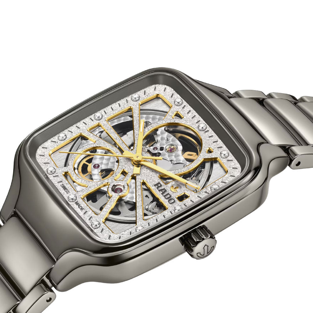 A close-up of the RADO True Square Automatic Open Heart Sparkling 38mm watch, a luxury timepiece with a high-tech ceramic case, skeleton dial with diamonds, gold and silver tones, visible internal mechanics, and a metallic bracelet.