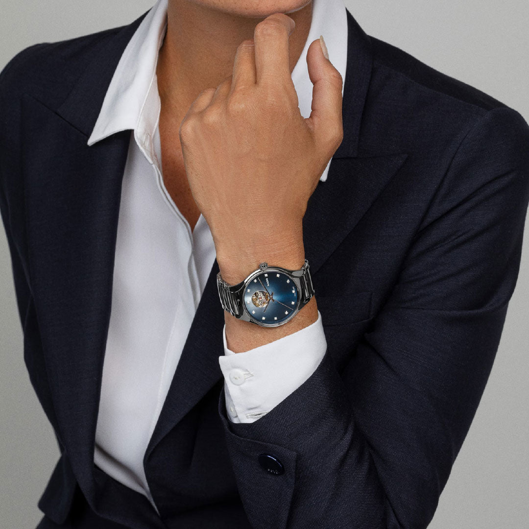 A person in a dark suit and white shirt rests their chin on their hand, wearing the RADO True Round Secret Diamonds Automatic 40mm Watch, featuring Swiss-made craftsmanship and intricate details by RADO.