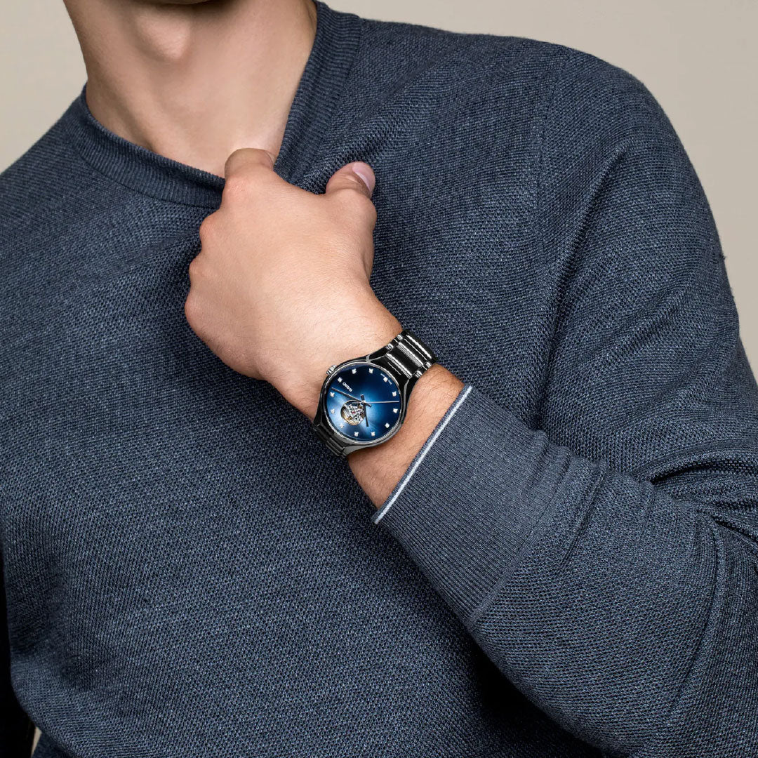 A person in a blue sweater adjusts their collar, showcasing a polished RADO True Round Secret Diamonds Automatic 40mm Watch with a blue face and Swiss-made movement.