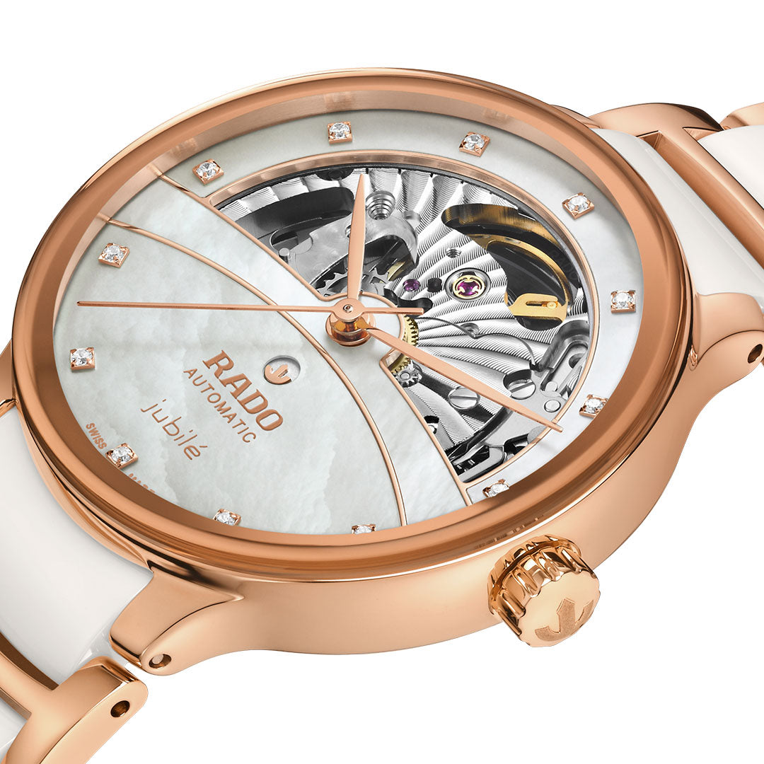 The RADO Centrix Automatic Diamonds Open Hearts 35mm Watch features a rose-gold PVD stainless steel and white ceramic band, a partially open skeleton dial with diamond hour markers, and visible intricate gears at the top.