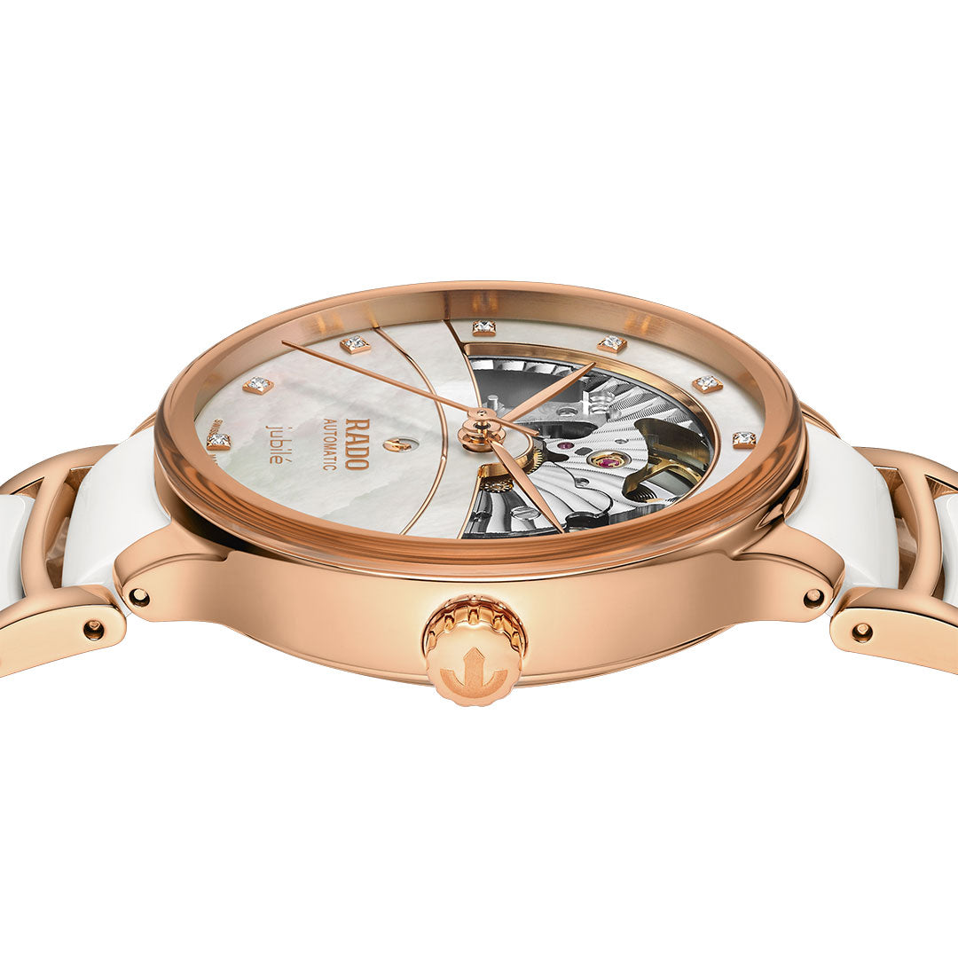 The RADO Centrix Automatic Diamonds Open Hearts 35mm Watch features a rose-gold PVD stainless steel and white ceramic band, a partially open skeleton dial with diamond hour markers, and visible intricate gears at the top.