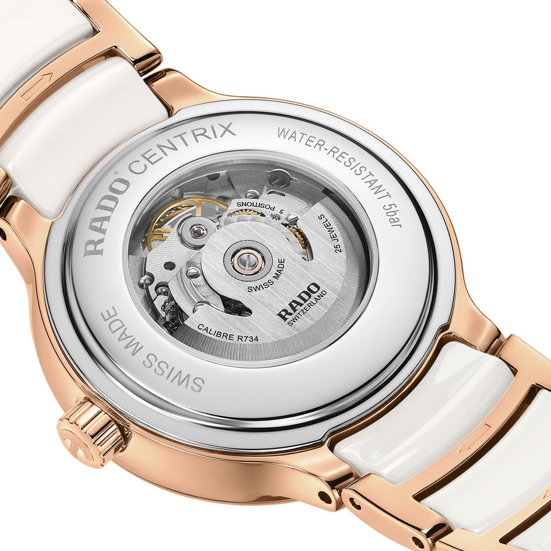 The RADO Centrix Automatic Diamonds Open Hearts 35mm Watch features a rose-gold PVD stainless steel and white ceramic band, a partially open skeleton dial with diamond hour markers, and visible intricate gears at the top.