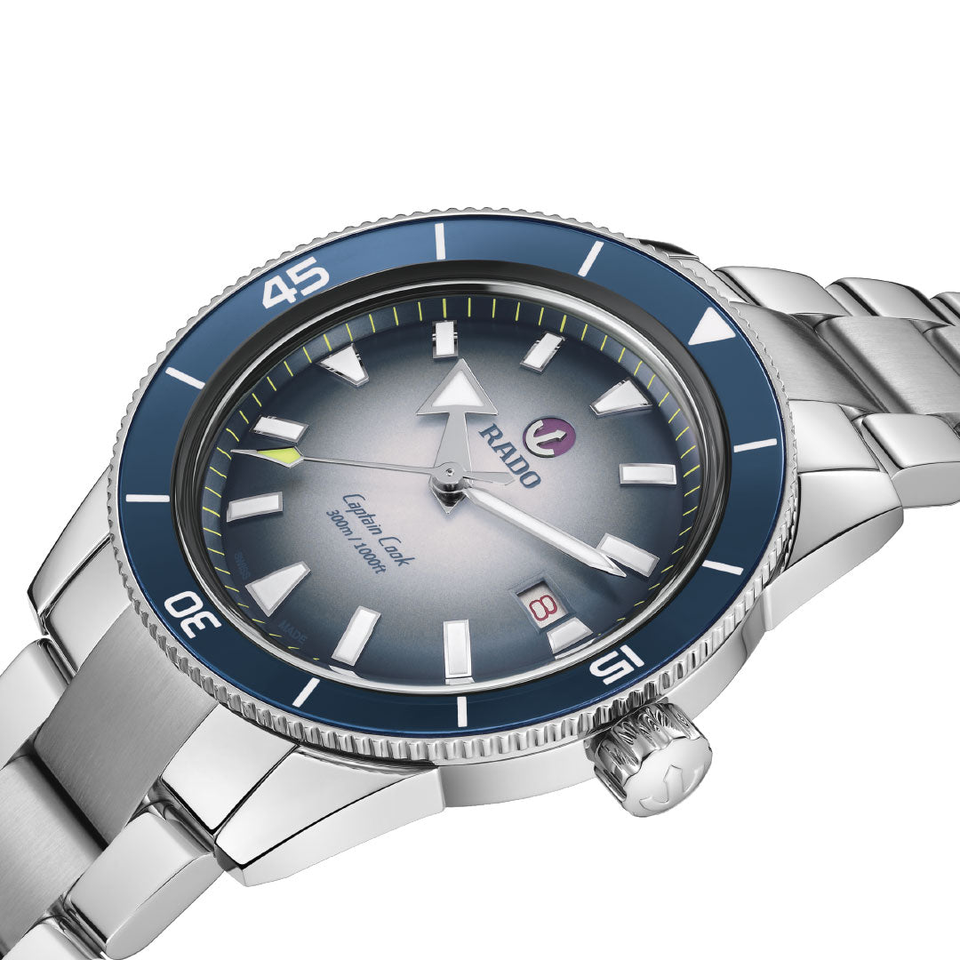 A close-up of the RADO Captain Cook Automatic 42mm Watch with a blue bezel, gradient blue dial, silver markers and hands, date window at 3 o’clock, 80-hour power reserve, and stainless steel bracelet.