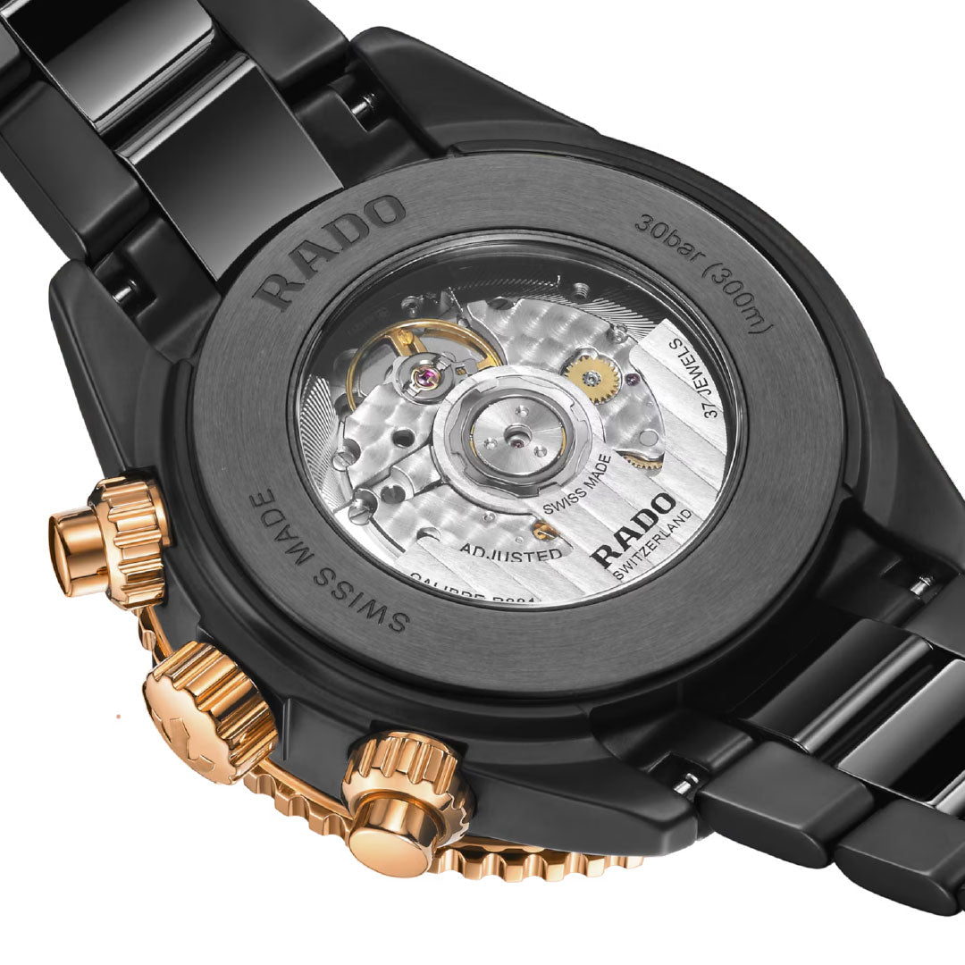 Close-up of the RADO Captain Cook High-Tech Ceramic Automatic Chronograph 43mm, showing its self-winding movement through the transparent caseback, with black and gold details, visible gears, and intricate engravings.