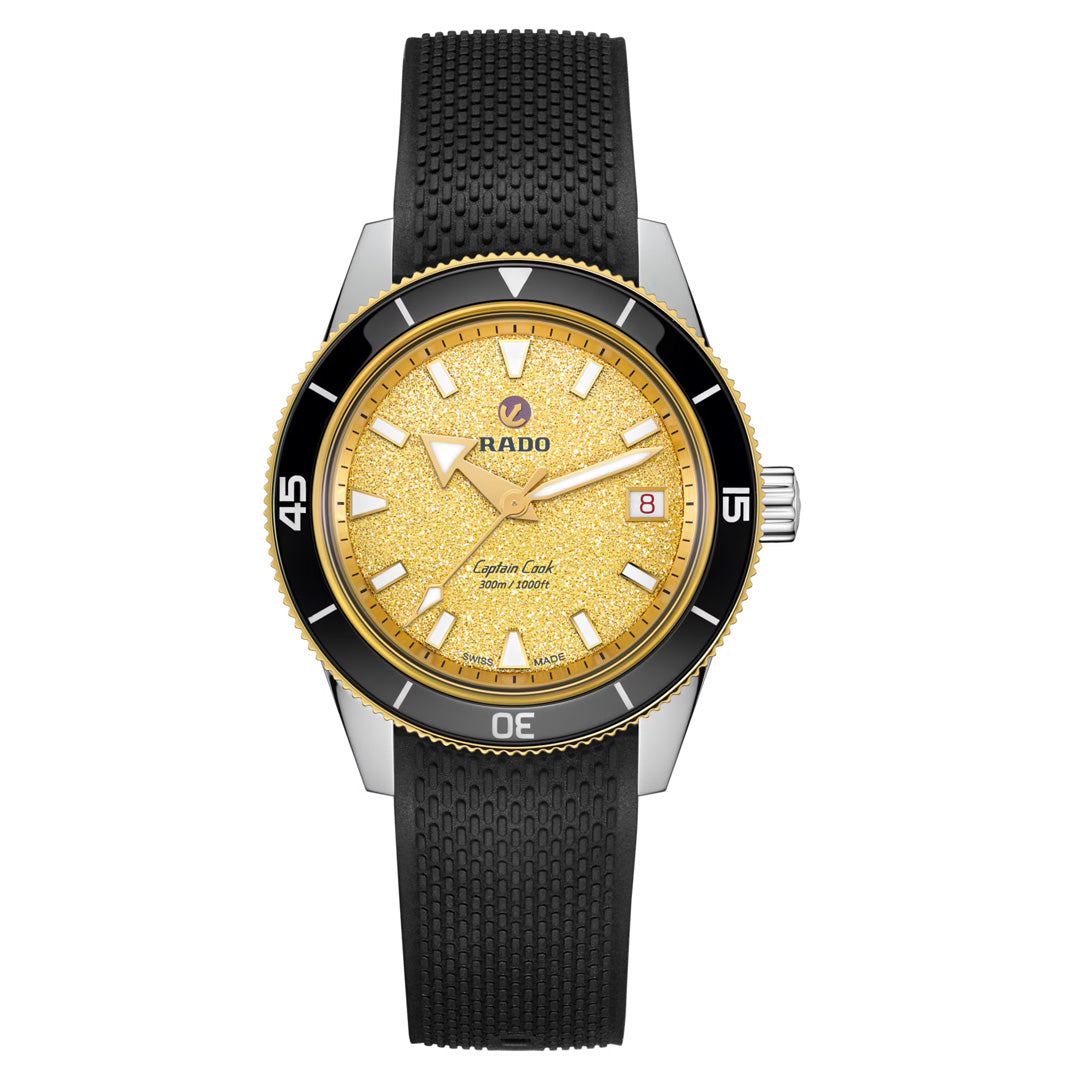 The RADO Captain Cook Automatic 39mm Watch features a gold-toned dial, black ceramic bezel, white hour markers with gold accents, a date display at 3 o’clock, and a textured black rubber strap.