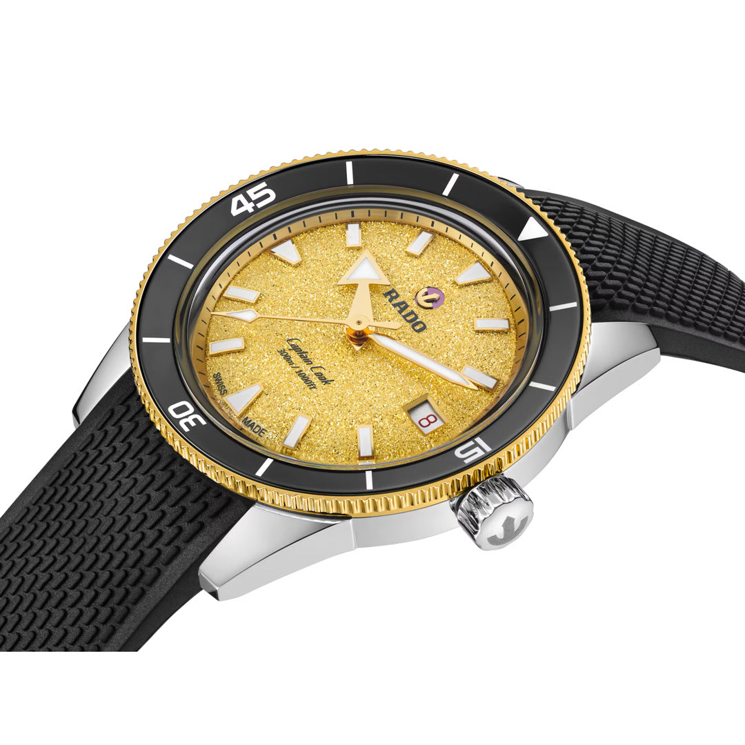 A close-up of the RADO Captain Cook Automatic 39mm Watch showcases its textured gold dial, black bezel, black strap, and silver case. This RADO timepiece features a date display along with bold white hour markers and hands.
