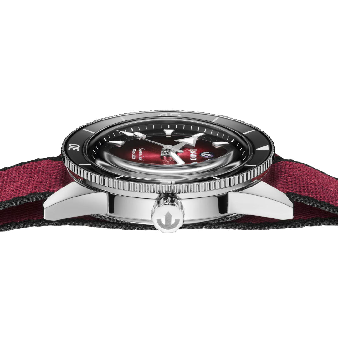 Side view of the RADO Captain Cook Automatic 39mm Watch featuring a polished silver case, black bezel, red fabric strap, anchor-engraved crown, and a slightly domed face revealing its automatic movement.
