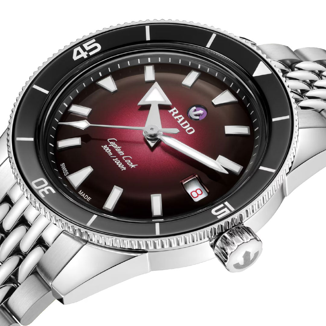 A close-up of the RADO Captain Cook Automatic 39mm Watch shows its metallic linked band, black bezel, gradient burgundy dial, luminous hands, automatic movement, and a crown with the signature RADO anchor logo.