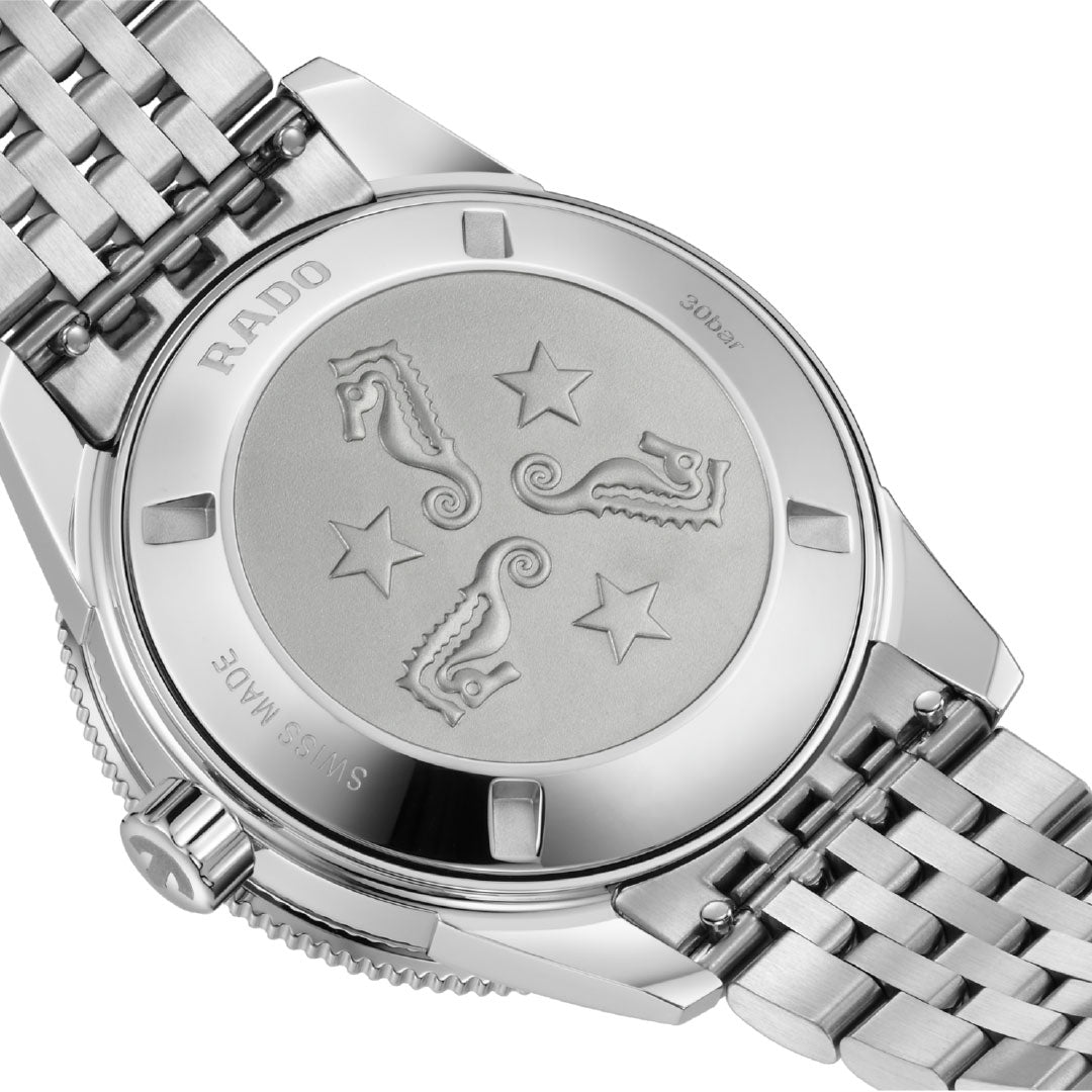 The back of the RADO Captain Cook Automatic 39mm Watch features an embossed design with three seahorses and stars. The silver metal bracelet, "Swiss Made" engraving, and automatic movement details are also visible.