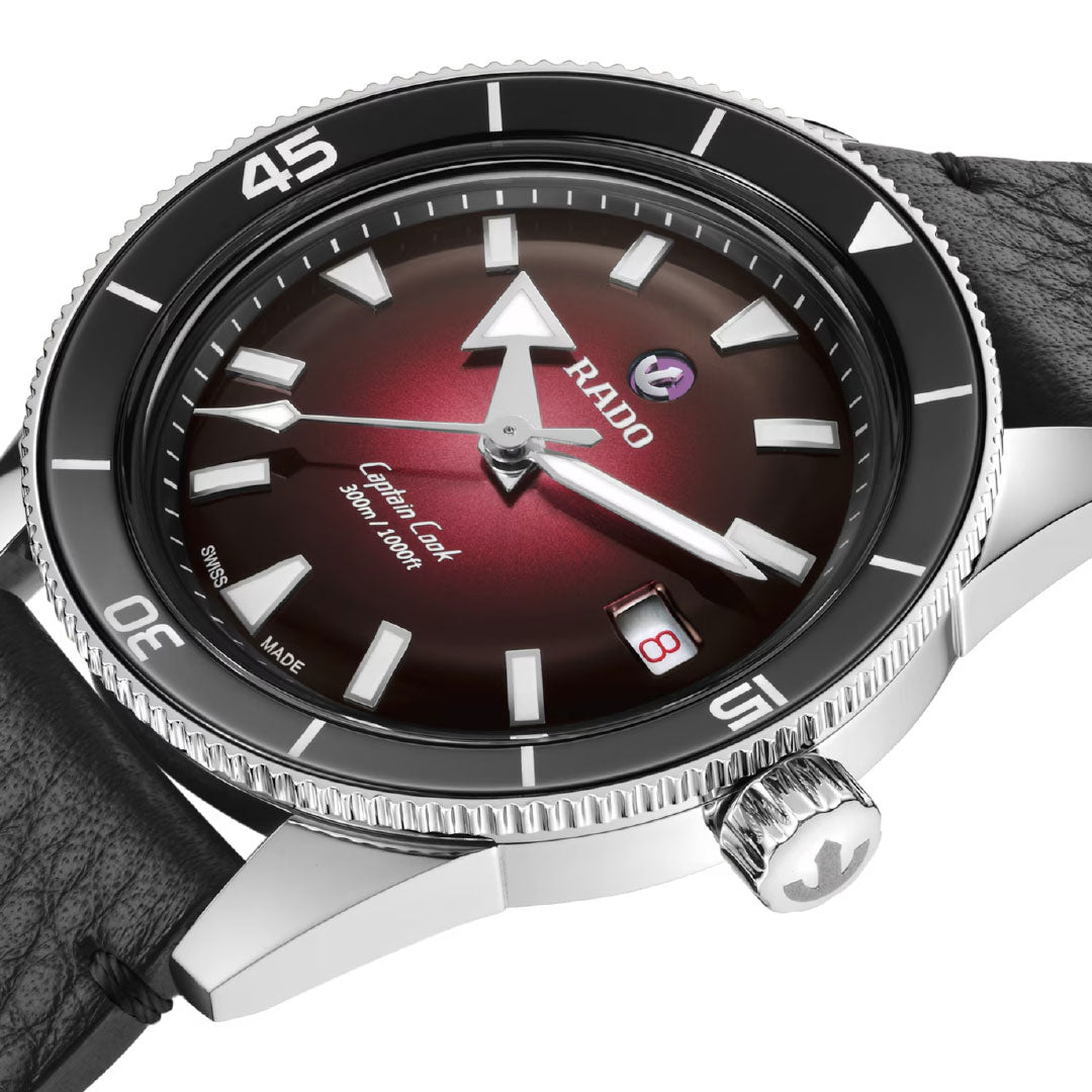 Close-up of the RADO Captain Cook Automatic 39mm Watch with a gradient red and black dial, silver markers, date display, black leather strap, and a black high-tech ceramic bezel with white numerals at 15, 30, and 45.