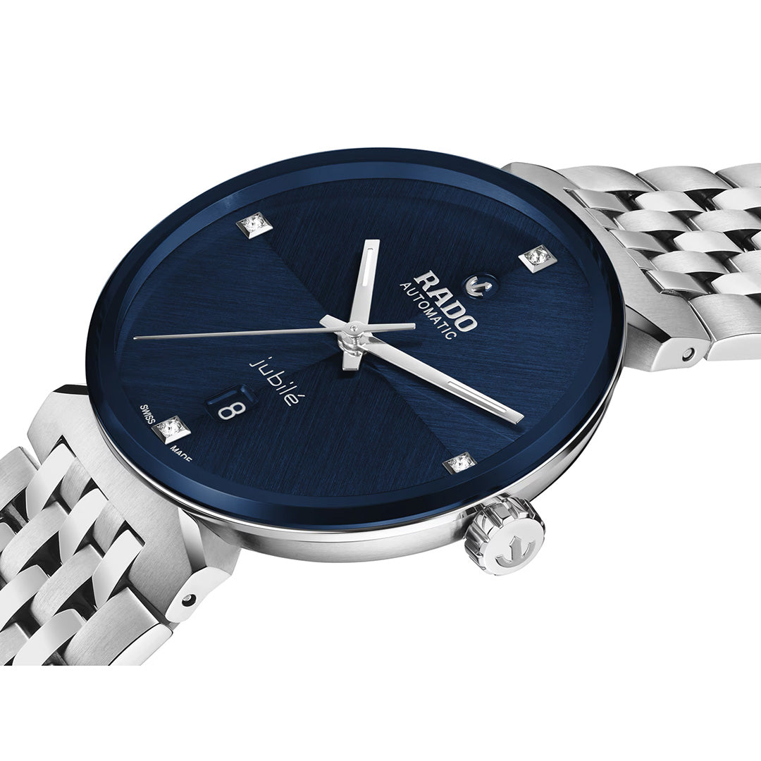 A silver RADO Florence Automatic 39mm watch with a blue dial, date display, diamond hour markers, and a metal link band is shown at an angle. This elegant Swiss-made timepiece by RADO features a durable sapphire crystal for lasting clarity.