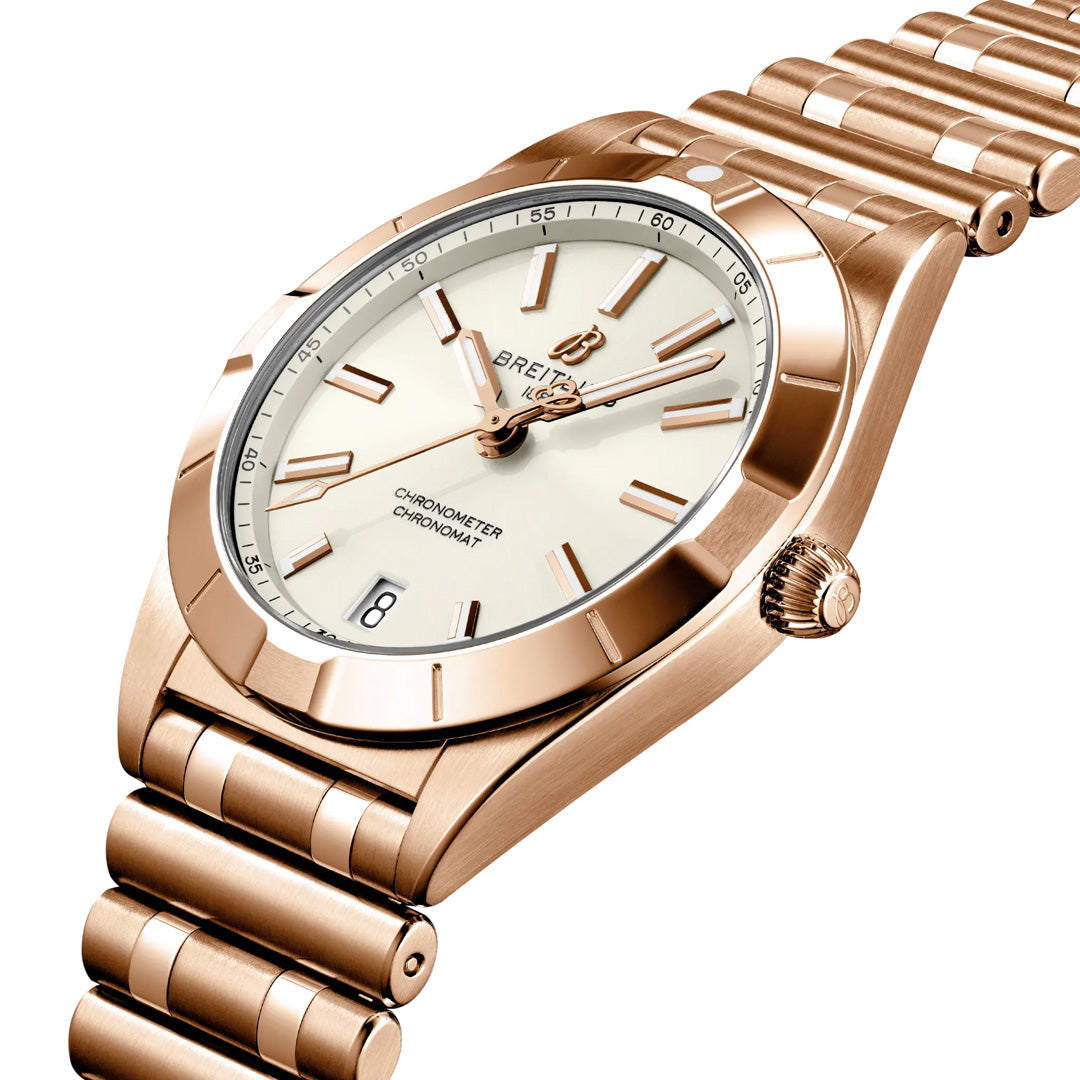 The BREITLING Chronomat 32 by Breitling is a luxurious women's gold watch featuring a white dial, gold hour markers, a date window at 6 o’clock, and a linked gold bracelet—shown here from a side angle. Powered by a precise SuperQuartz chronometer movement, this elegant timepiece seamlessly combines sophistication and performance.