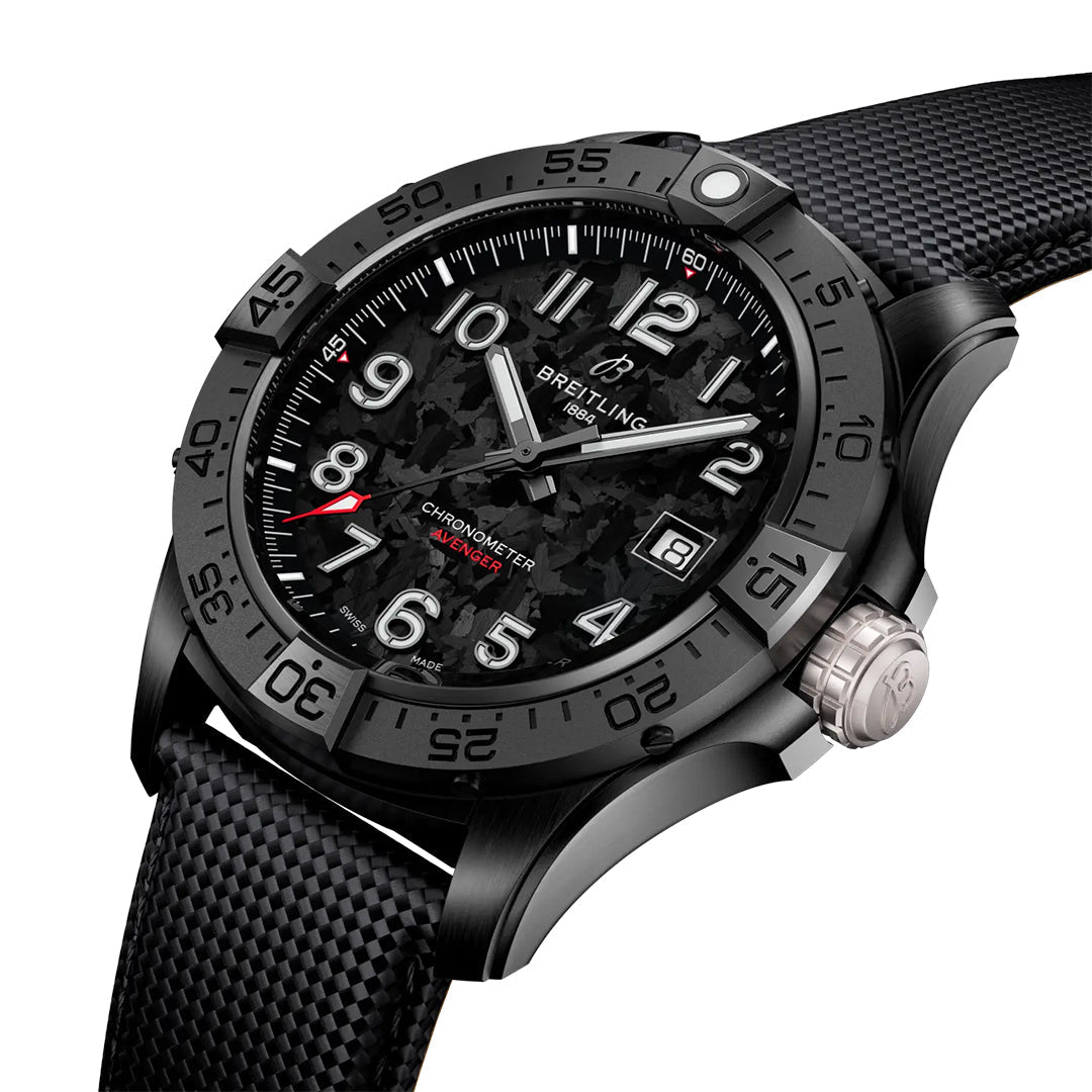 The BREITLING Avenger Automatic 42 Night Mission features a textured carbon fiber dial with white numerals, a red minute hand with a circular tip, and an aviation-inspired black bezel and metallic crown. A black textured strap complements the design, while the Breitling name is visible on the dial.