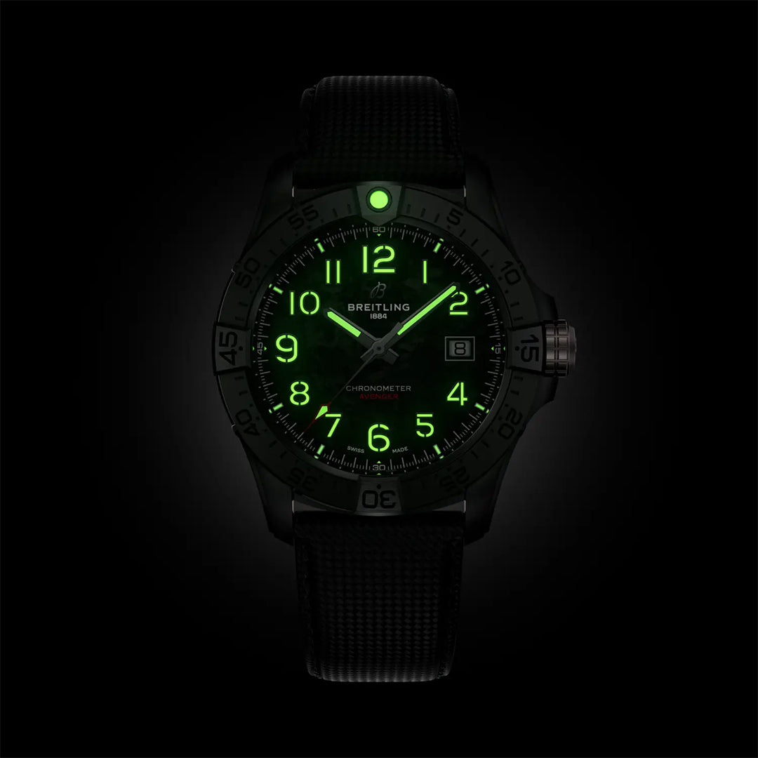 The BREITLING Avenger Automatic 42 Night Mission features a black case with a glowing green aviation-themed dial. The watch boasts luminous Arabic numerals, hands, and a date window on the right. Complemented by a military leather strap, the watch embodies Breitling's dark Avenger appeal.