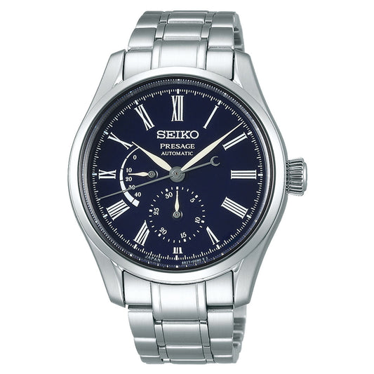 The Seiko Presage Craftsmanship Series Automatic with Manual Winding 40.5mm Watch features a striking blue enamel dial complemented by black Roman numerals, a date display, and a small seconds sub-dial. The elegant design includes a silver stainless steel band and is set against a plain white background.