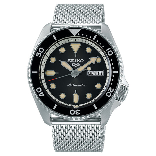 The Seiko 5 Sports SKX Series Automatic 42.5mm Watch from Seiko features a stainless steel mesh band and case, a sophisticated black dial, a day and date display on the right side, luminous hour markers, and a unidirectional bezel with minute markings for precise timing.