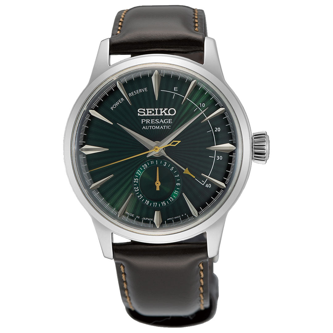 A Seiko Presage Cocktail Time Automatic watch with a manual winding mechanism showcases a dark green textured dial, silver-tone markers, and hands. It features a power reserve indicator and subdial, while the black leather strap is enhanced with light brown stitching for an exquisite blend of style and functionality.