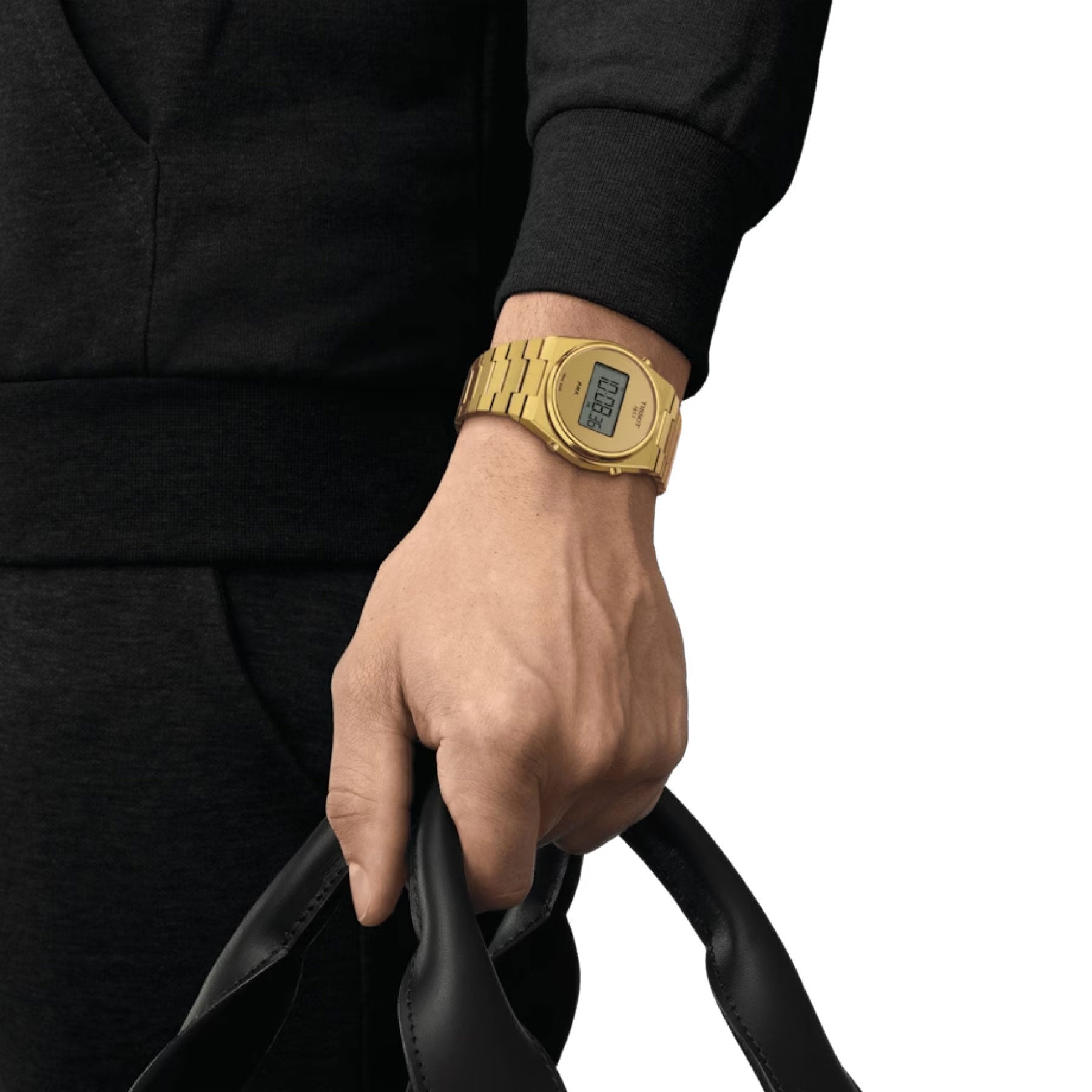 A person dressed in a black outfit holds a black bag, adorned with a Tissot PRX Digital Quartz 40mm Watch, featuring a rectangular gold digital display. The sophisticated elegance of Swiss Quartz technology is striking against the plain white background.