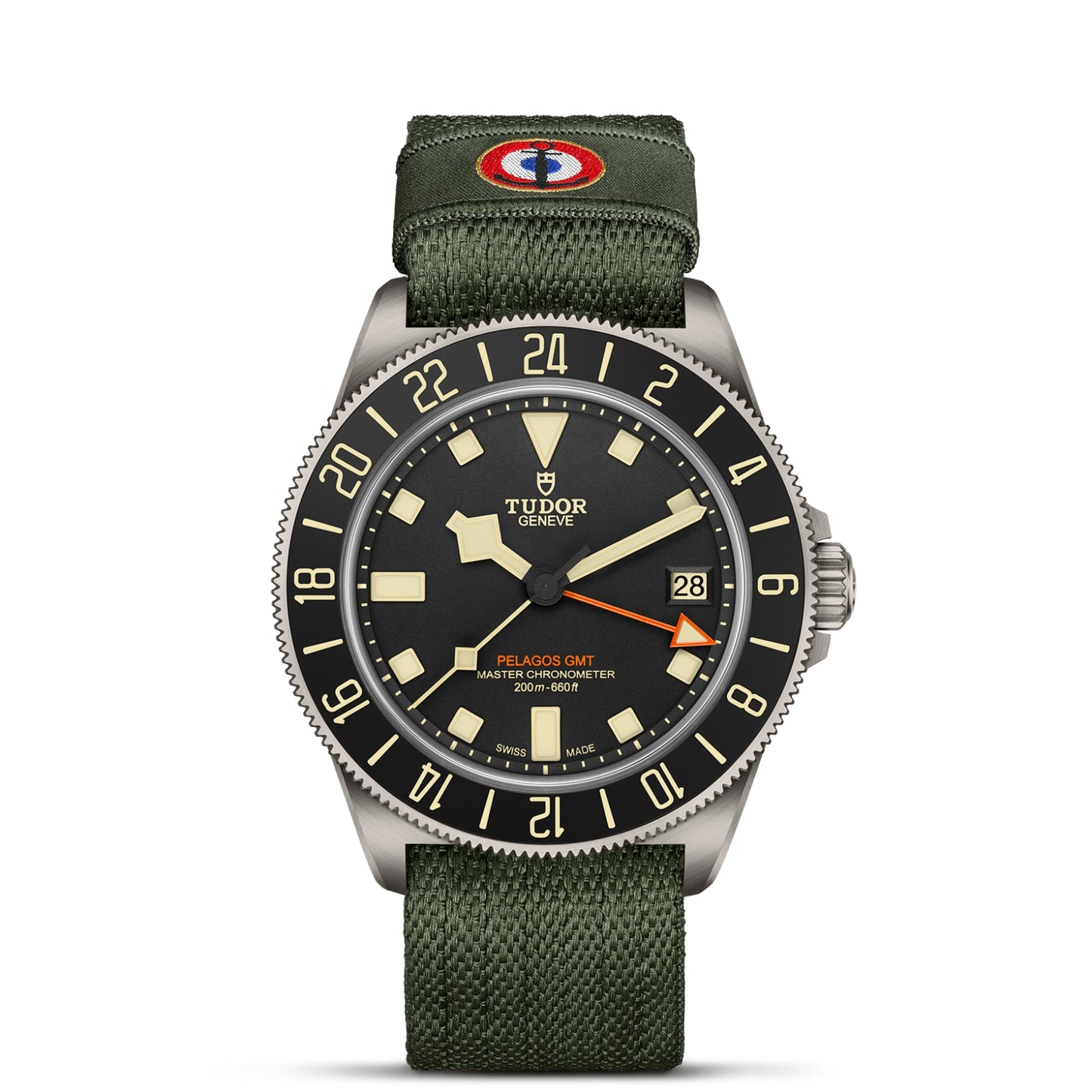 The TUDOR Pelagos FXD GMT features a black dial, beige markers, date display, black and beige 24-hour bezel, and olive green fabric strap with a red, white, and blue patch inspired by French Naval Aviation and Zulu time.
