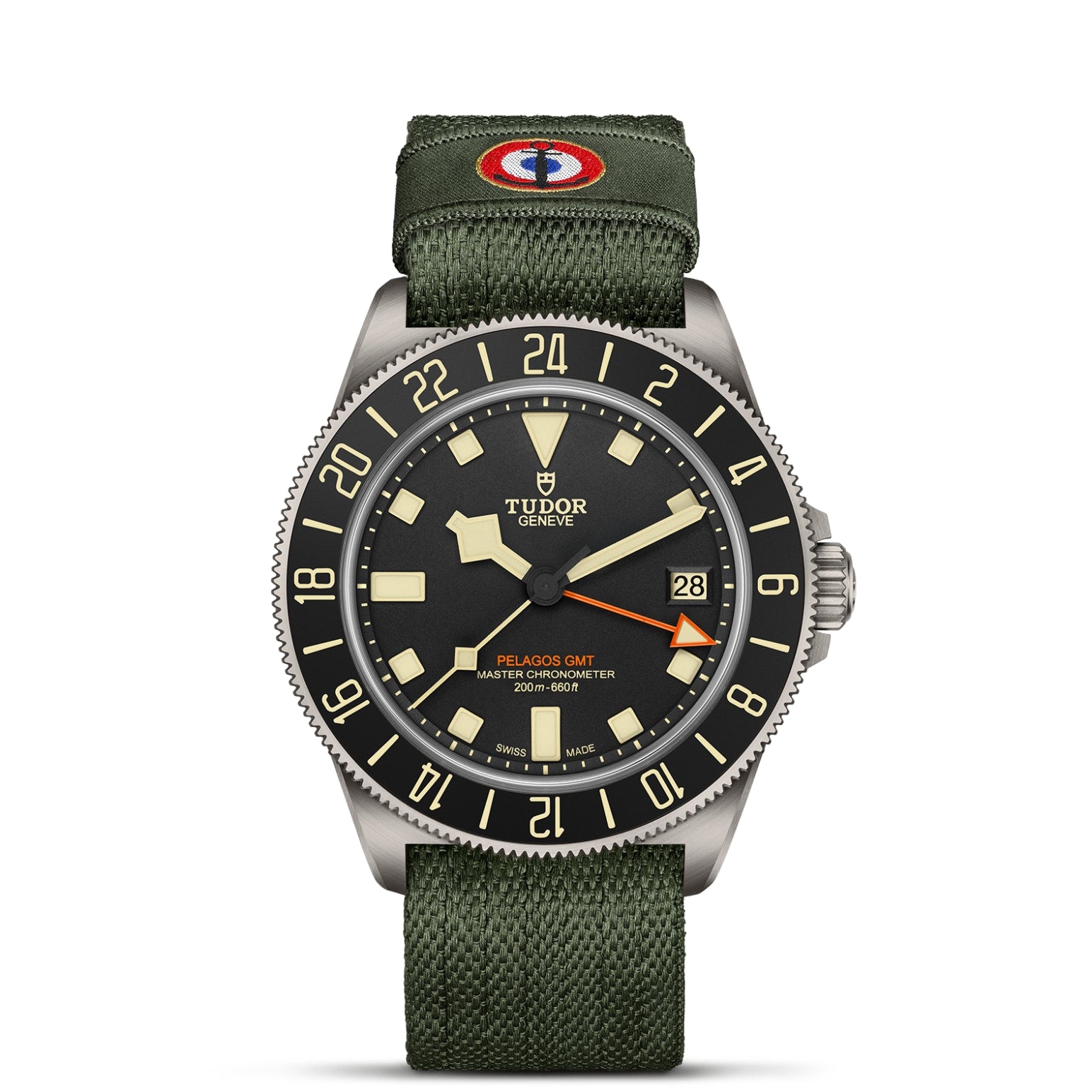 The TUDOR Pelagos FXD GMT features a black dial, beige markers, date display, black and beige 24-hour bezel, and olive green fabric strap with a red, white, and blue patch inspired by French Naval Aviation and Zulu time.