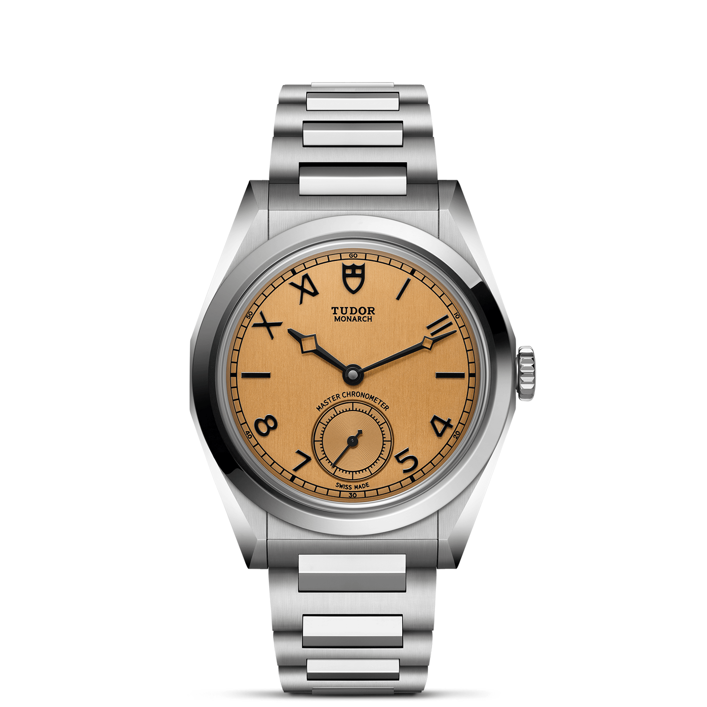 The TUDOR Monarch features a stainless steel case, light brown dial with black Arabic numerals, small seconds at 6 o’clock, and a brushed metal bracelet. The iconic TUDOR logo is positioned below 12 o’clock.