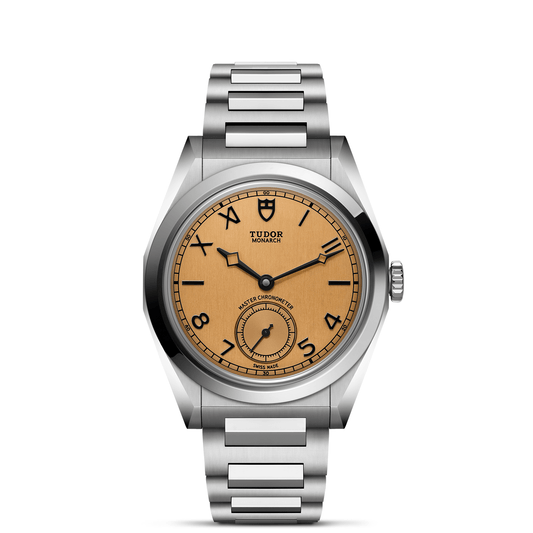The TUDOR Monarch features a stainless steel case, light brown dial with black Arabic numerals, small seconds at 6 o’clock, and a brushed metal bracelet. The iconic TUDOR logo is positioned below 12 o’clock.