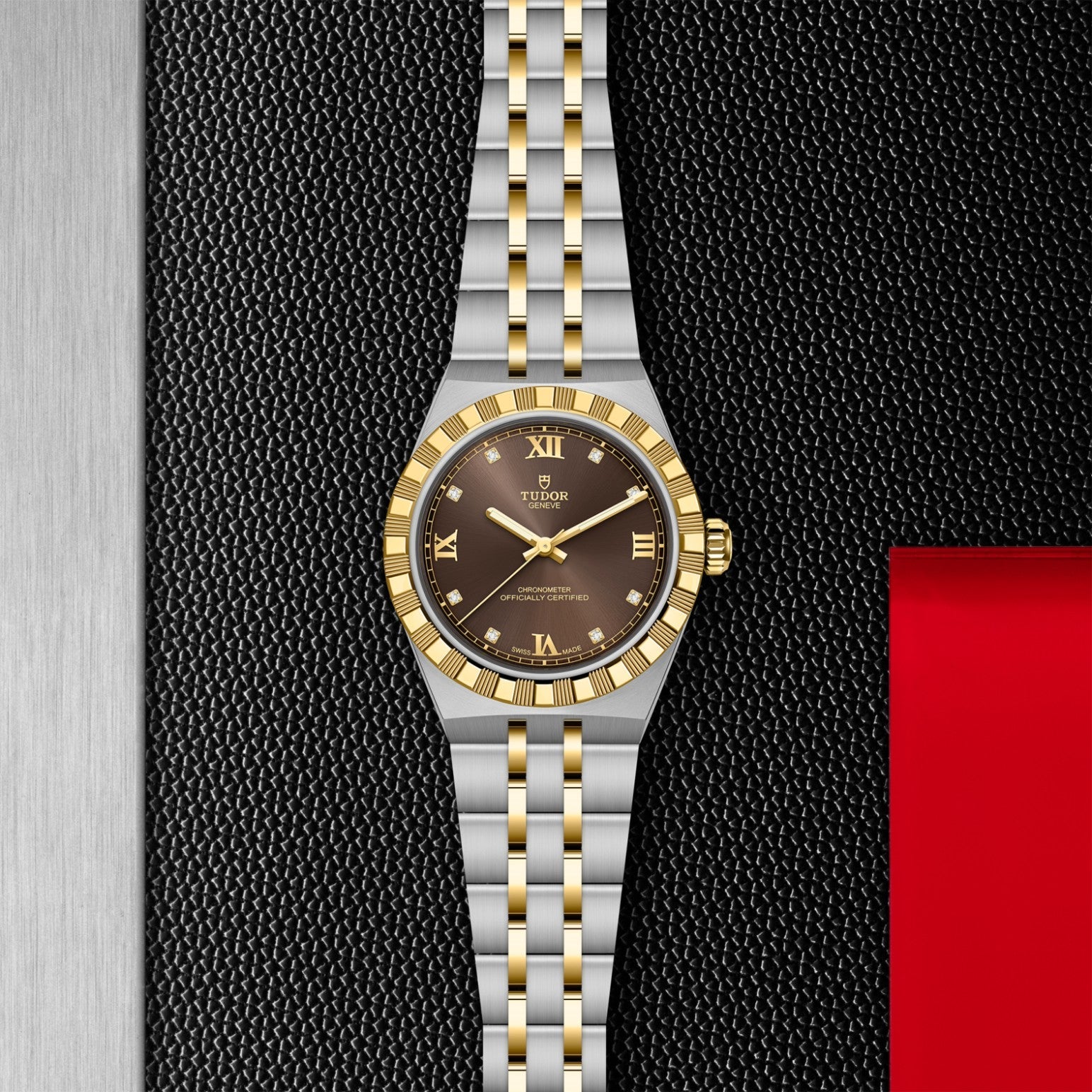 The TUDOR Royal by TUDOR features a two-tone gold and silver bracelet, a gold bezel, and a black Roman numeral dial, displayed on a textured black surface with metallic and red accents—embodying sporty elegance.
