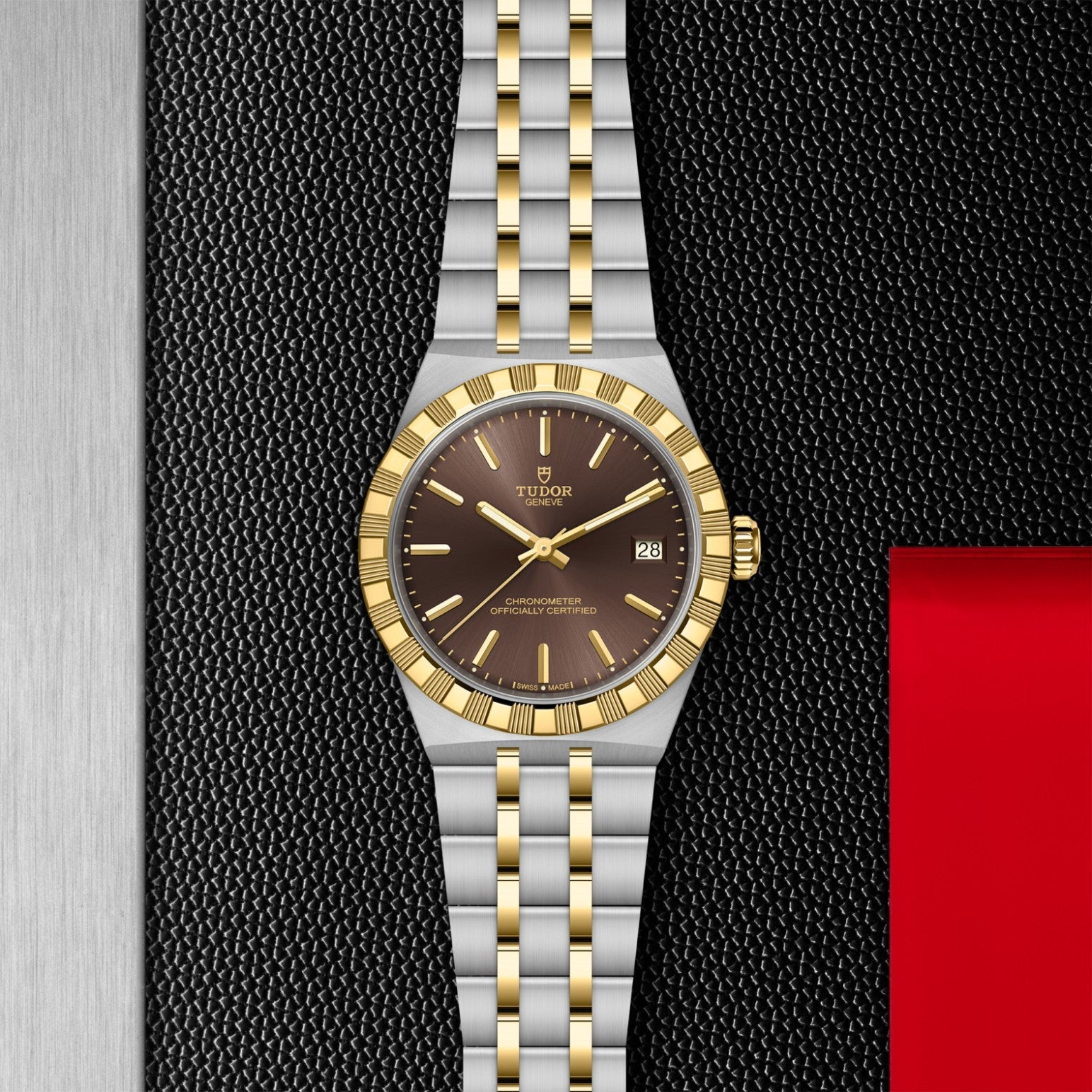 The TUDOR Royal by TUDOR features a gold and silver bracelet, gold bezel, and brown dial with date display, shown against a textured black background with red and silver accents.