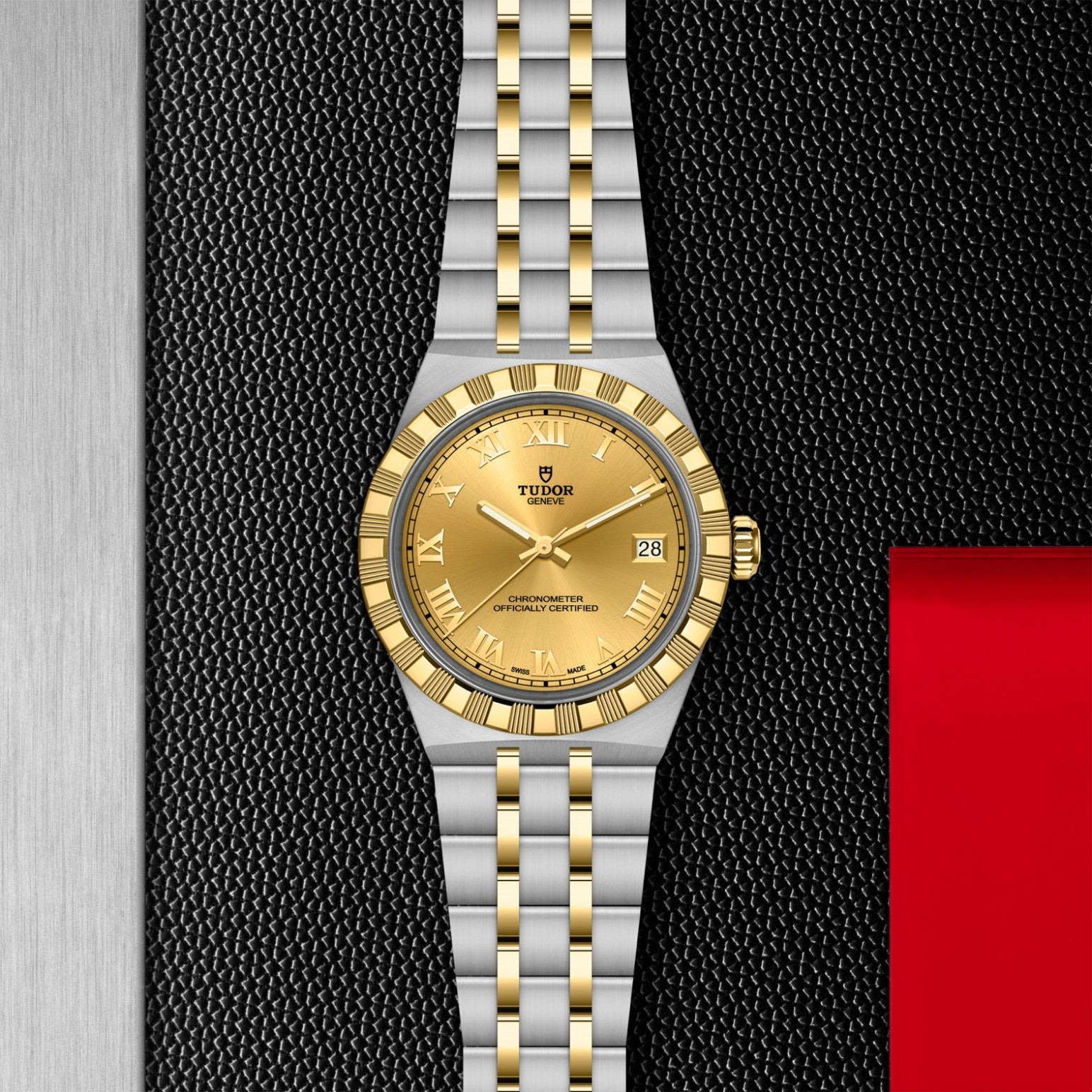 A TUDOR Royal wristwatch by TUDOR, featuring a gold dial, gold bezel, and a silver-and-gold bracelet, is showcased on a textured black surface with metallic and red accents in the background.