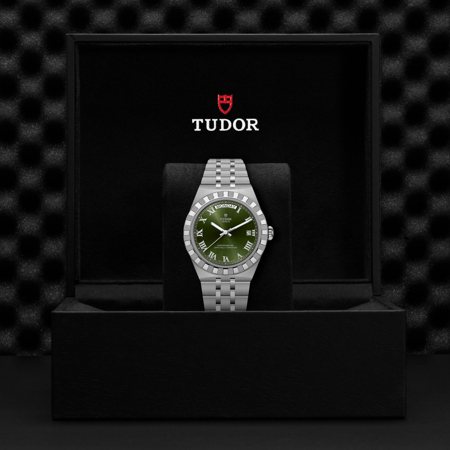 A TUDOR Royal wristwatch with a green dial and Roman numerals is showcased in an open black box, featuring the red and white TUDOR logo above this striking stainless steel timepiece.