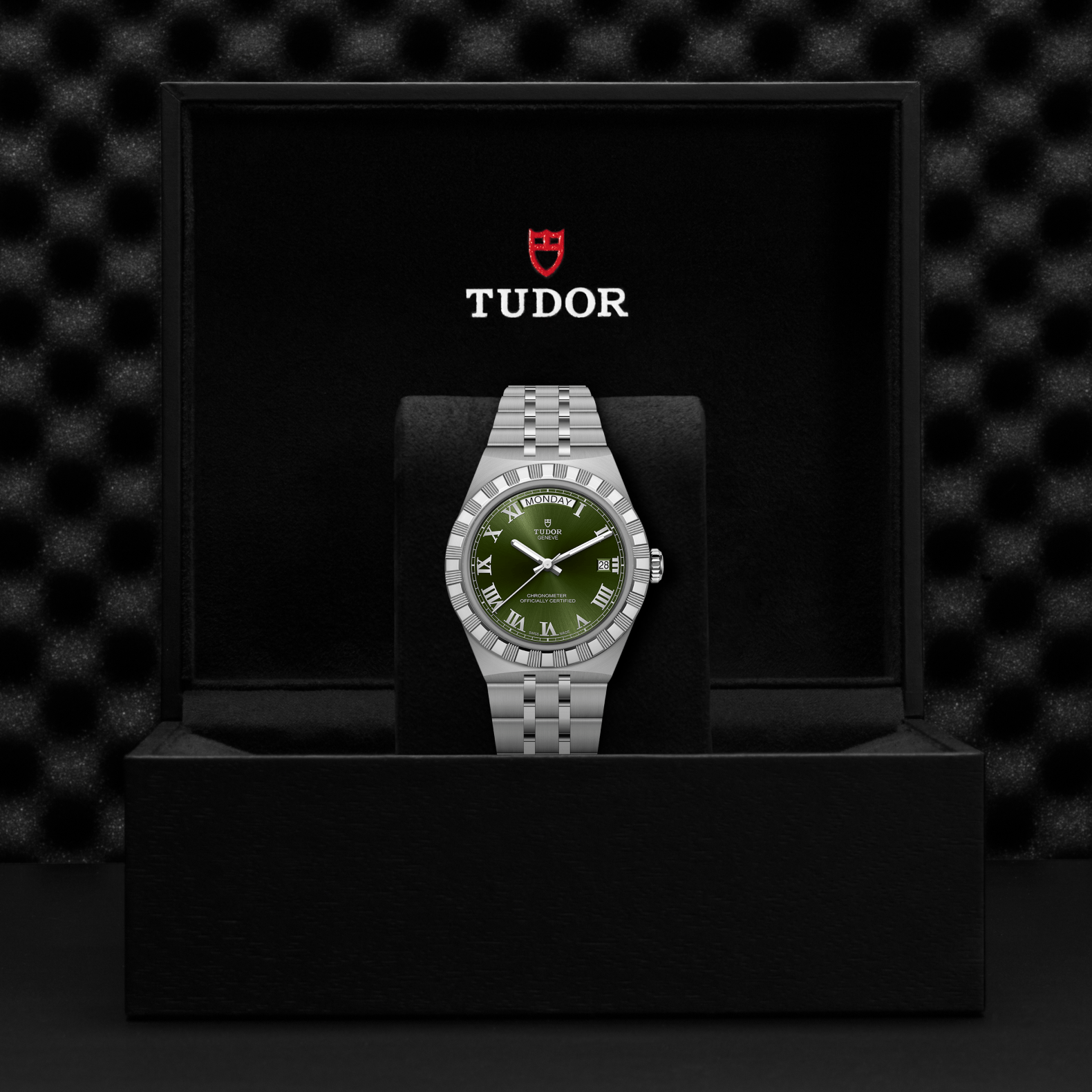 A TUDOR Royal wristwatch with a green dial and Roman numerals is showcased in an open black box, featuring the red and white TUDOR logo above this striking stainless steel timepiece.
