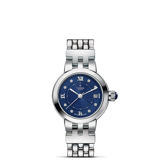 A TUDOR Clair de Rose silver wristwatch with an opaline dial, blue lacquered Roman numerals, diamond hour markers, a date at 3 o'clock, and a linked metal band is displayed against a white background.