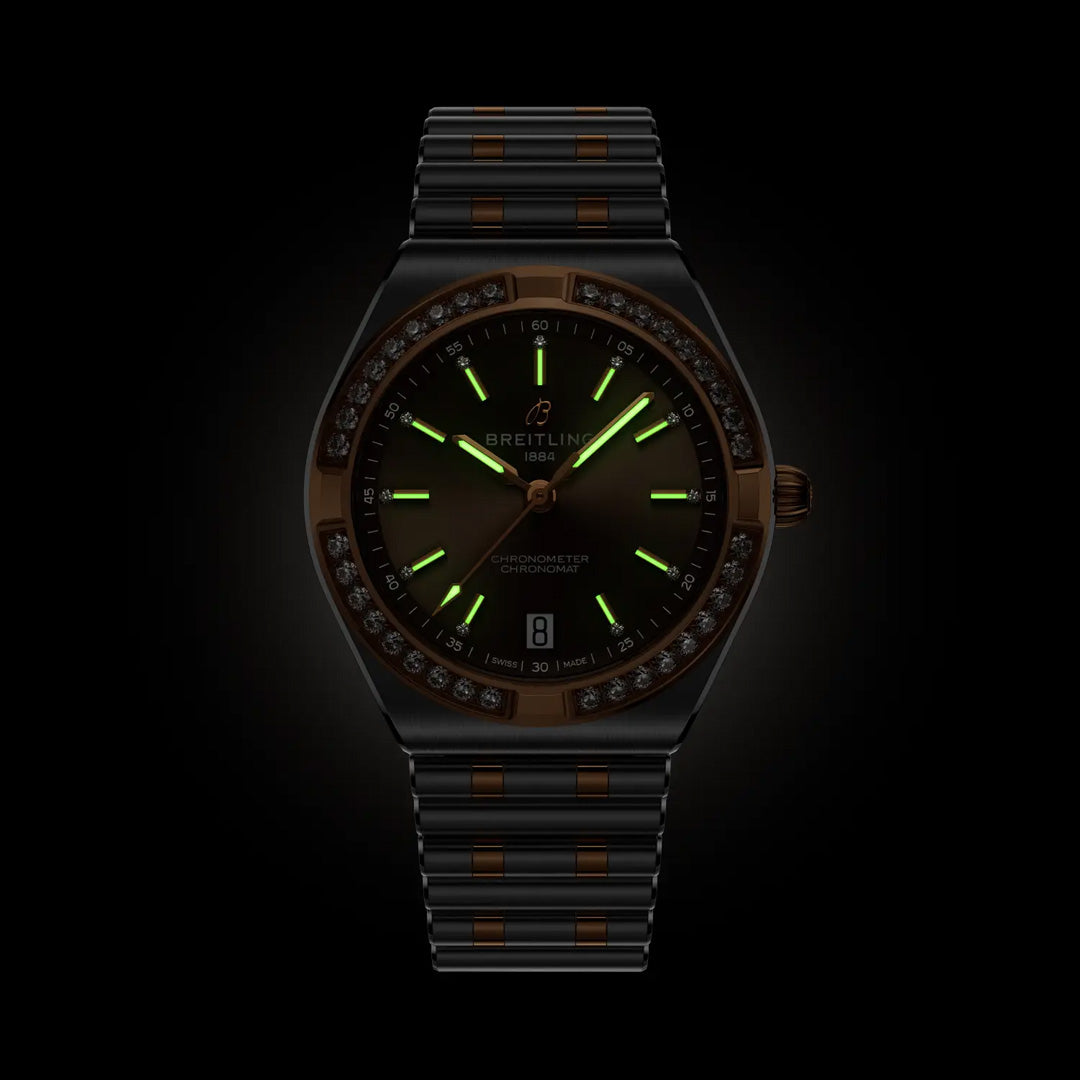 The BREITLING Chronomat Automatic 36 is a black sports watch with a dark face, glowing green markers and hands, and a matching metal strap, all shown against a black background.