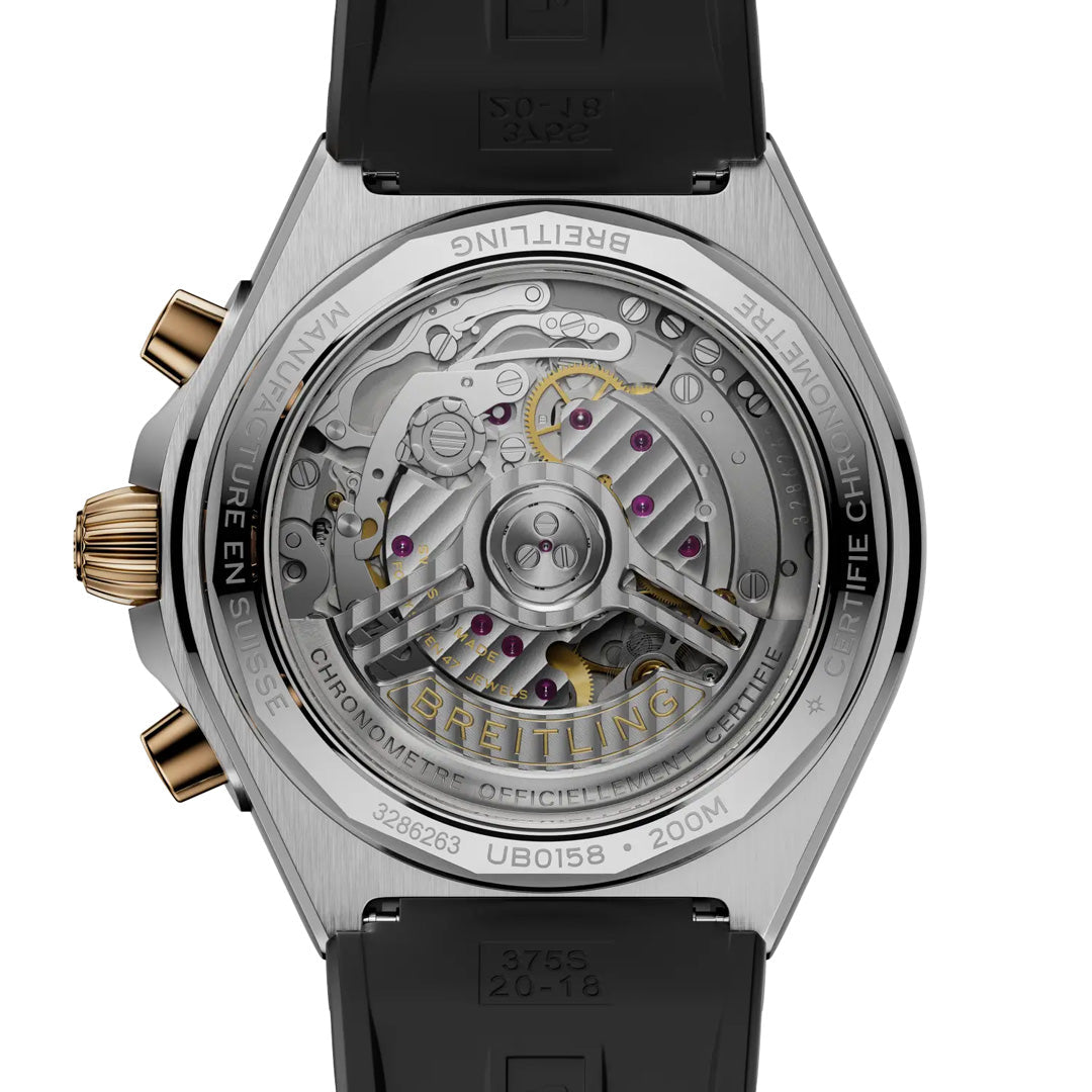 Close-up of the BREITLING Chronomat B01 Chronograph 42's back, revealing its detailed automatic movement with visible gears and rotor. The stainless steel case boasts engraved branding, while the black rubber strap is partially visible. Brand: Breitling.