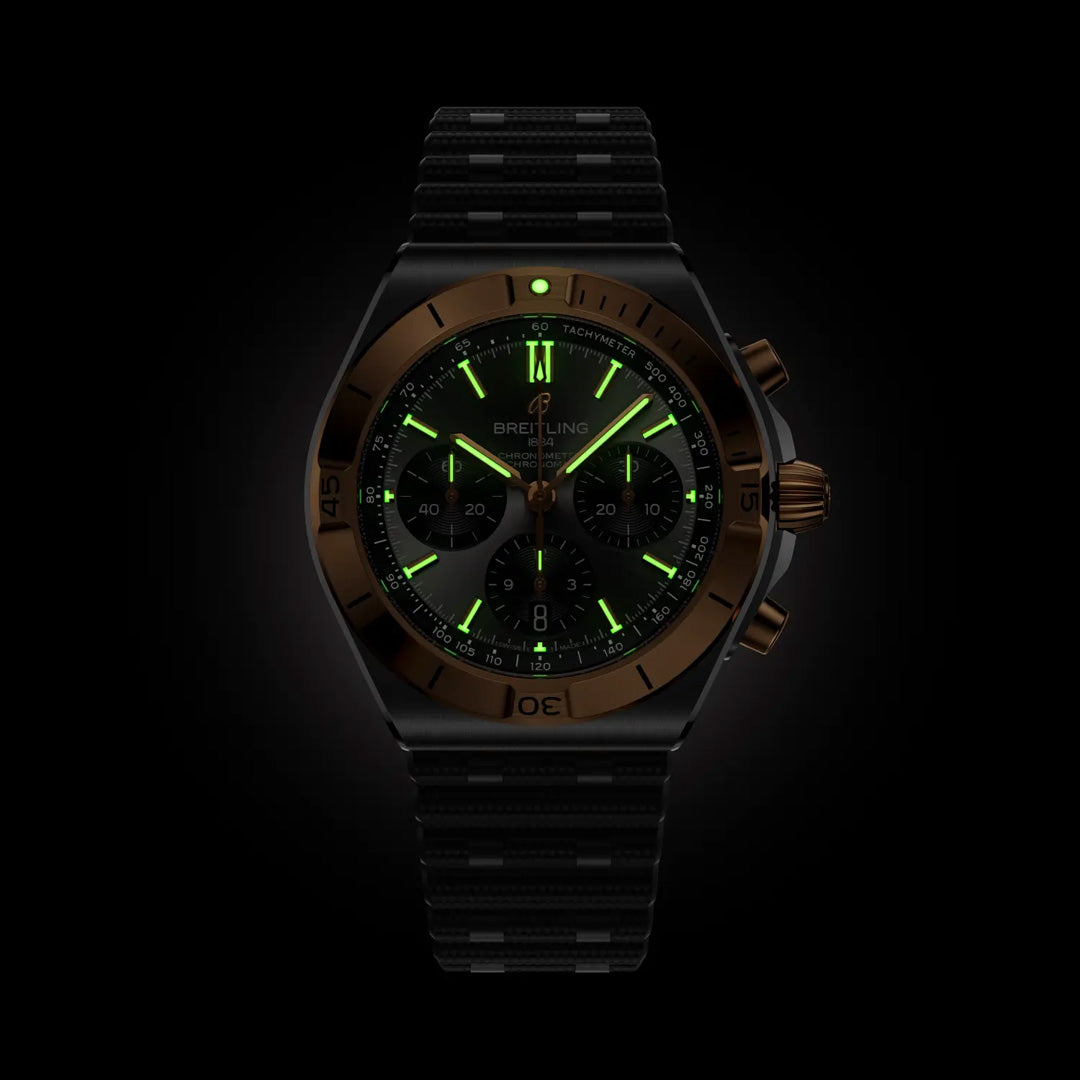 The Breitling Chronomat B01 Chronograph 42 features a black sports design with a dark bezel and luminous green hour markers and hands, shown glowing against a black background.