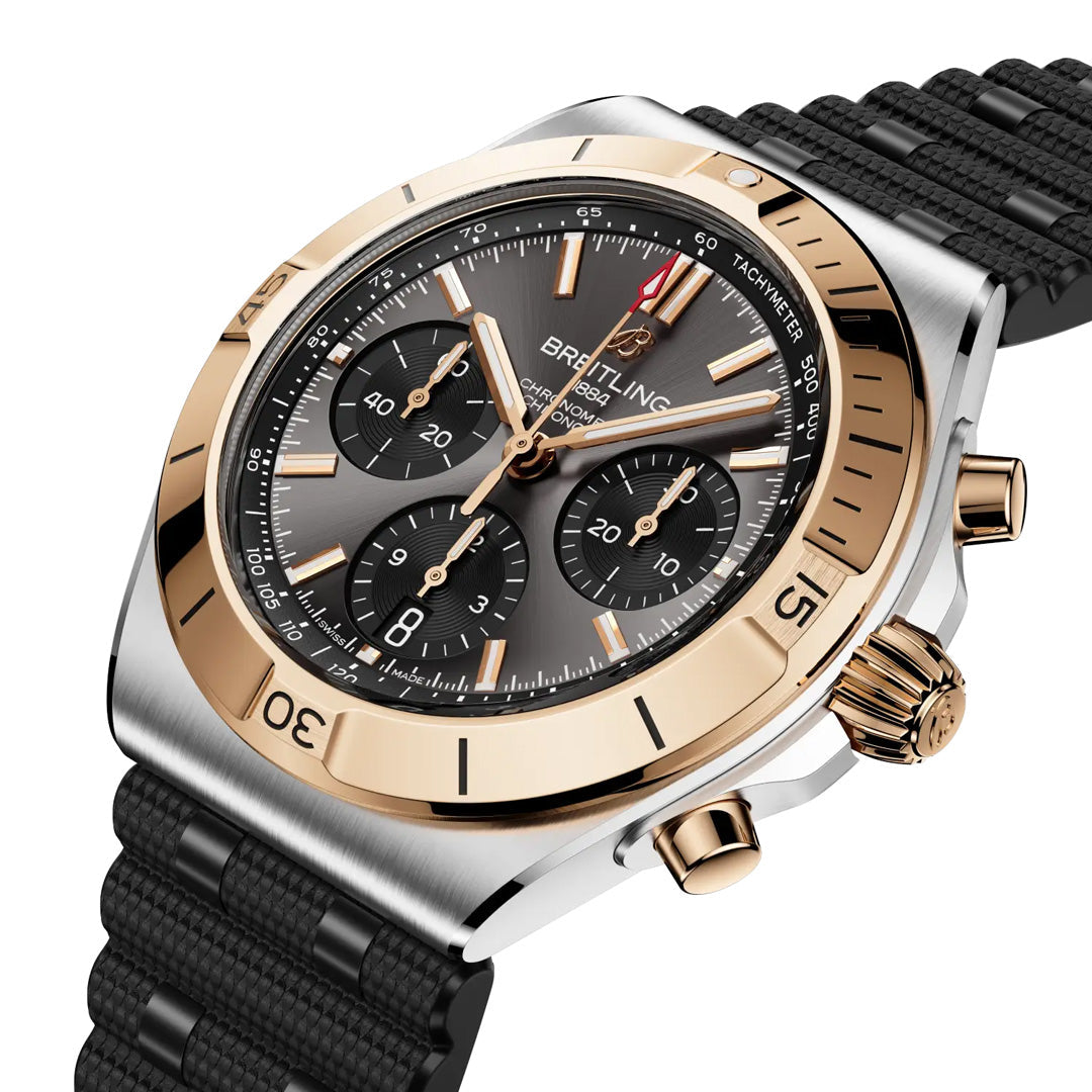 The BREITLING Chronomat B01 Chronograph 42 is a luxury sports watch by Breitling with a black textured strap, gold bezel engraved with numbers, and a black dial featuring three chronograph subdials, gold accents, and bold hour markers.