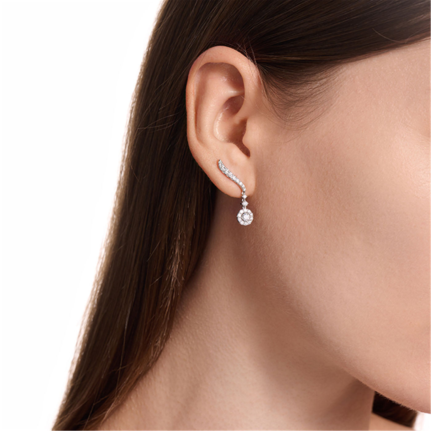 A close-up highlights a woman's ear graced by the Hearts On Fire Vela 18K White Gold Drop Earrings. Her dark brown hair is straight and tucked behind her ear against a white background, enhancing the elegance of this exquisite piece from Hearts on Fire's fine jewelry collection.